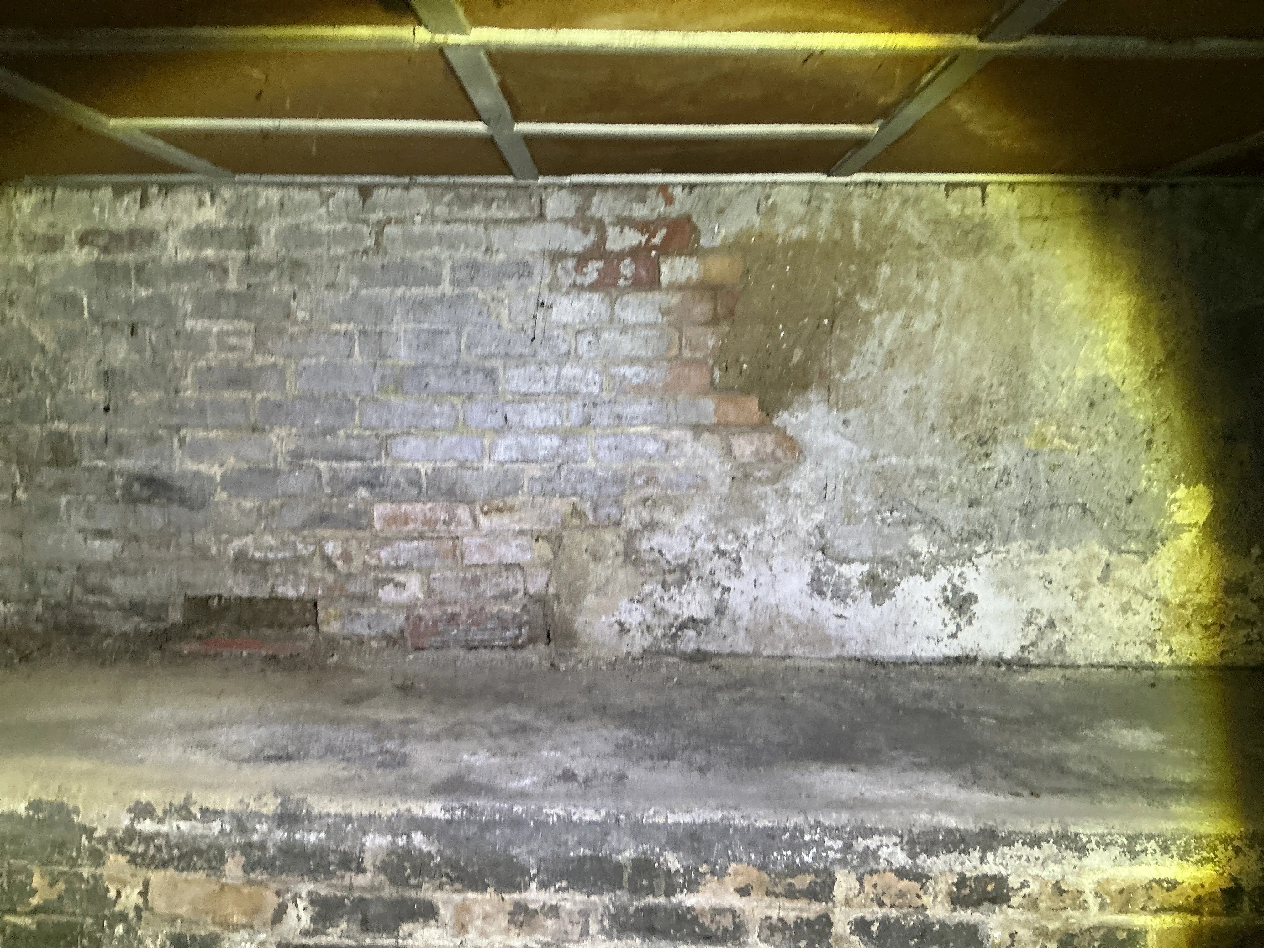 Exposed brick foundation wall with damaged plaster render in a home crawl space 2026-07-06