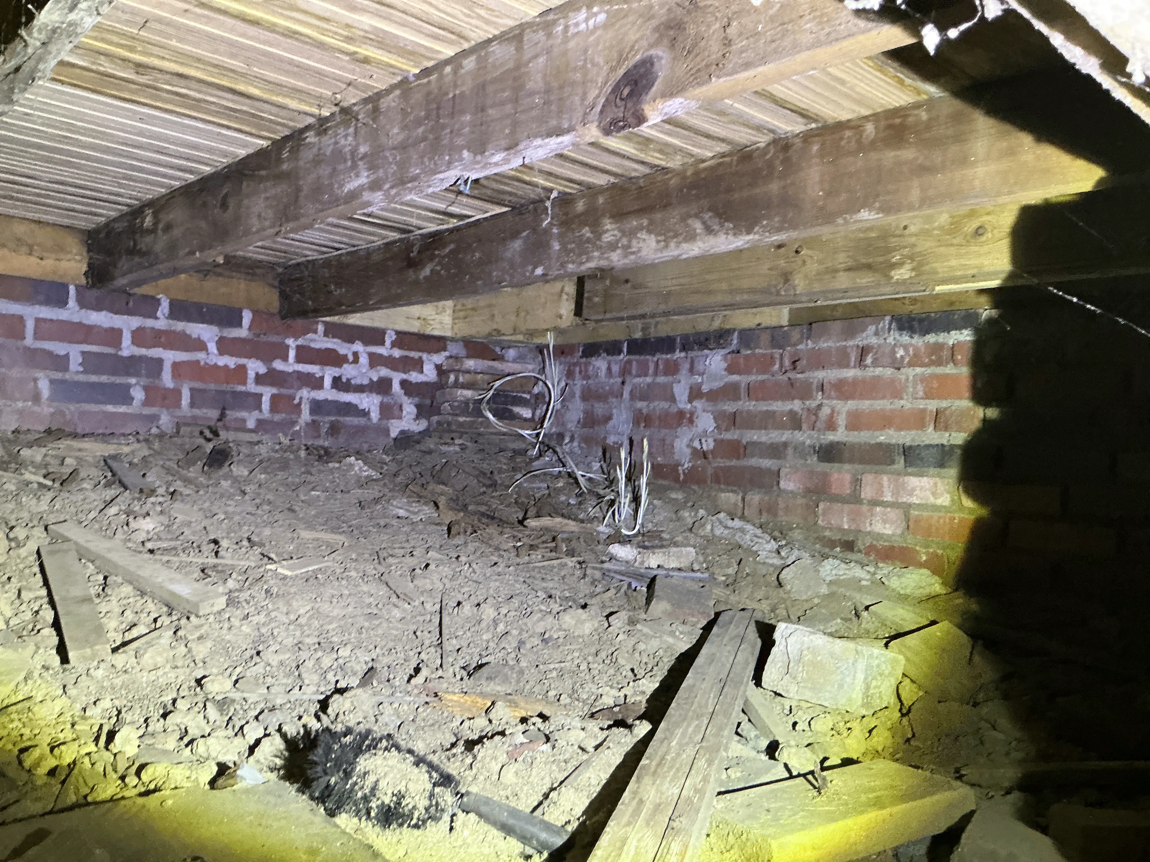 Crawlspace inspection showing dirt floor with debris, exposed electrical wires, brick foundation, and wooden floor joists. 2026-07-14