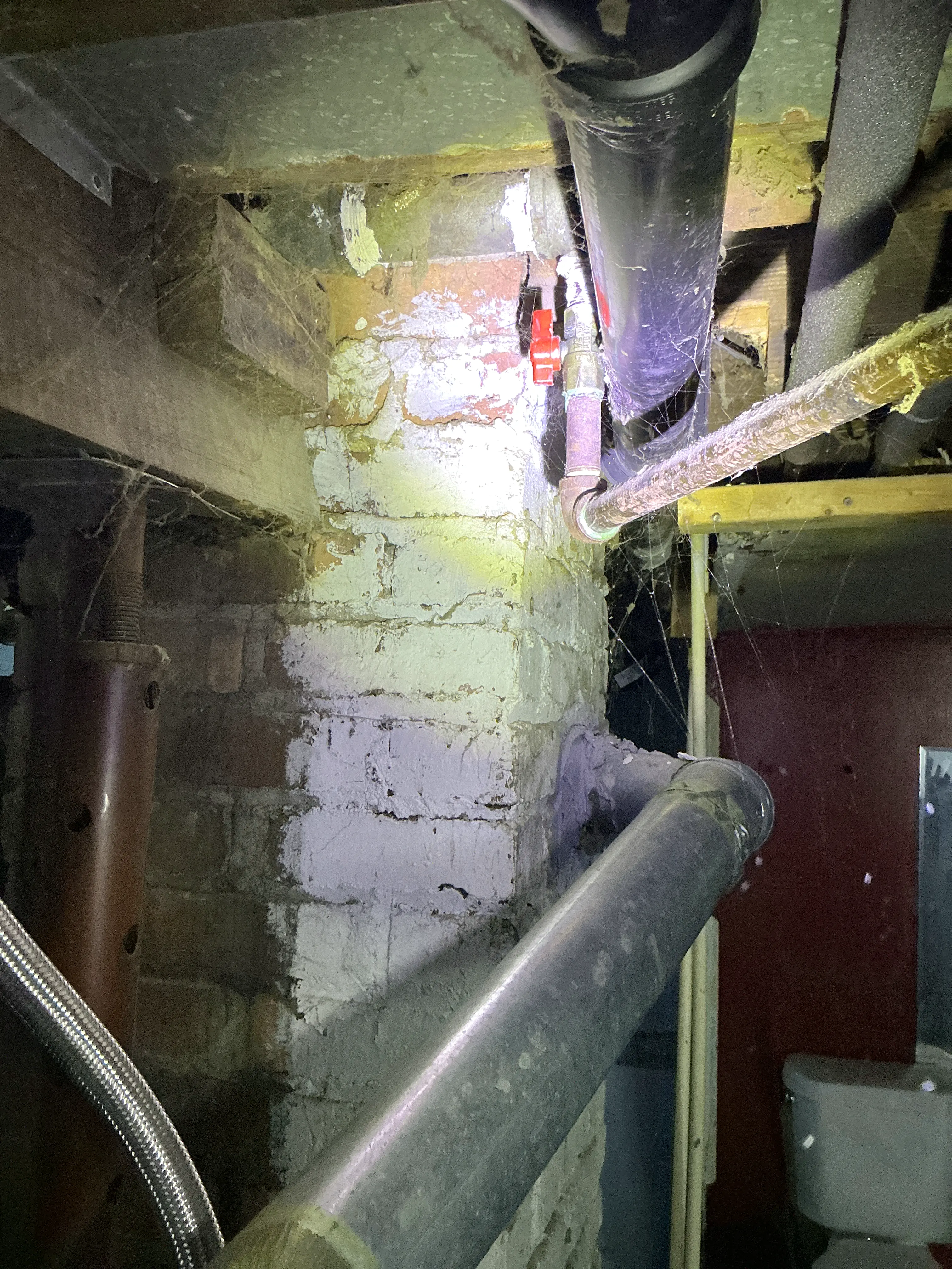 Exposed plumbing pipes, shutoff valve, and brick foundation wall in a basement during a lead inspection 2026-08-03