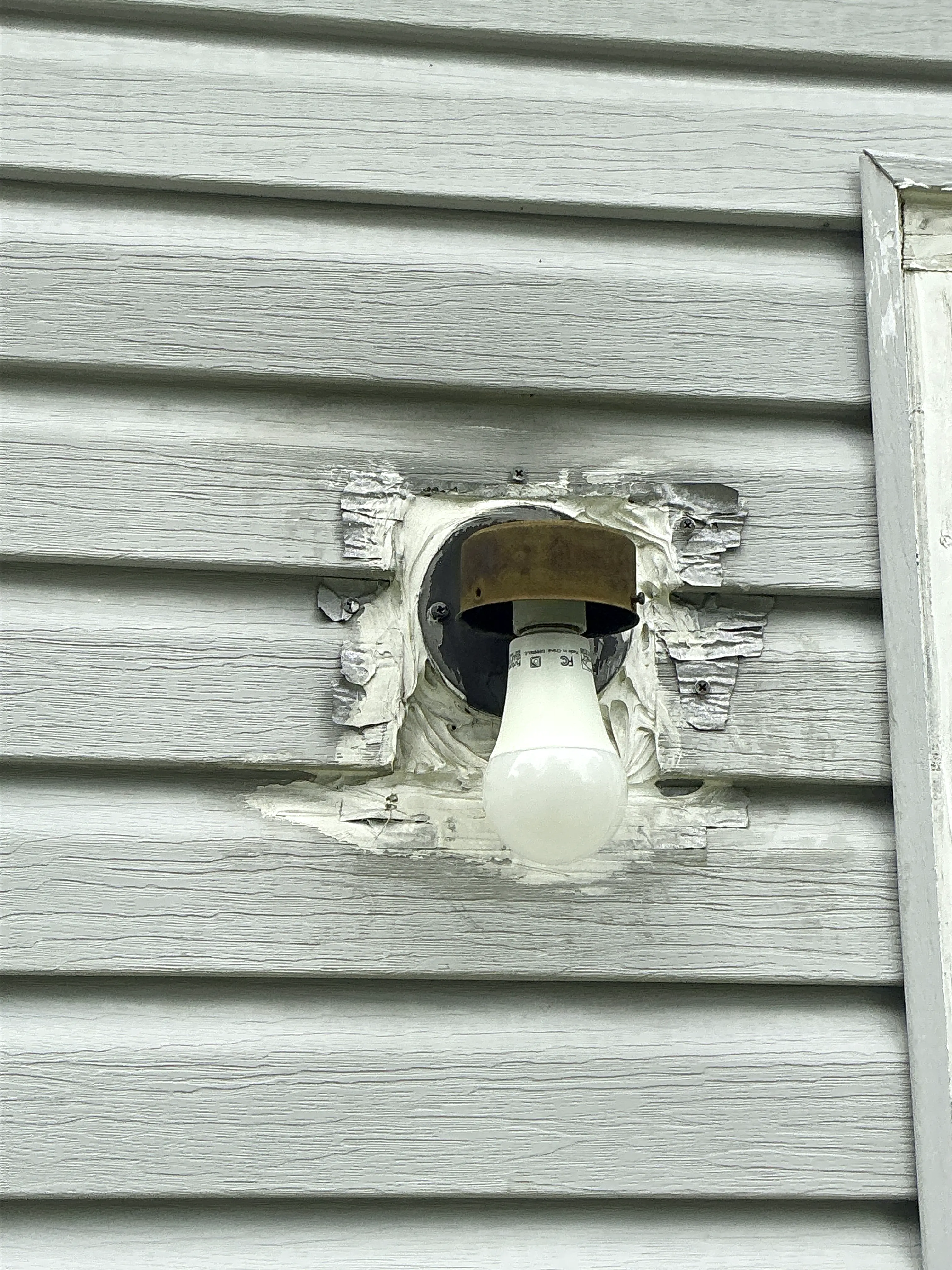 Damaged exterior light fixture mounted on vinyl siding without a globe or fixture cover 2026-08-22