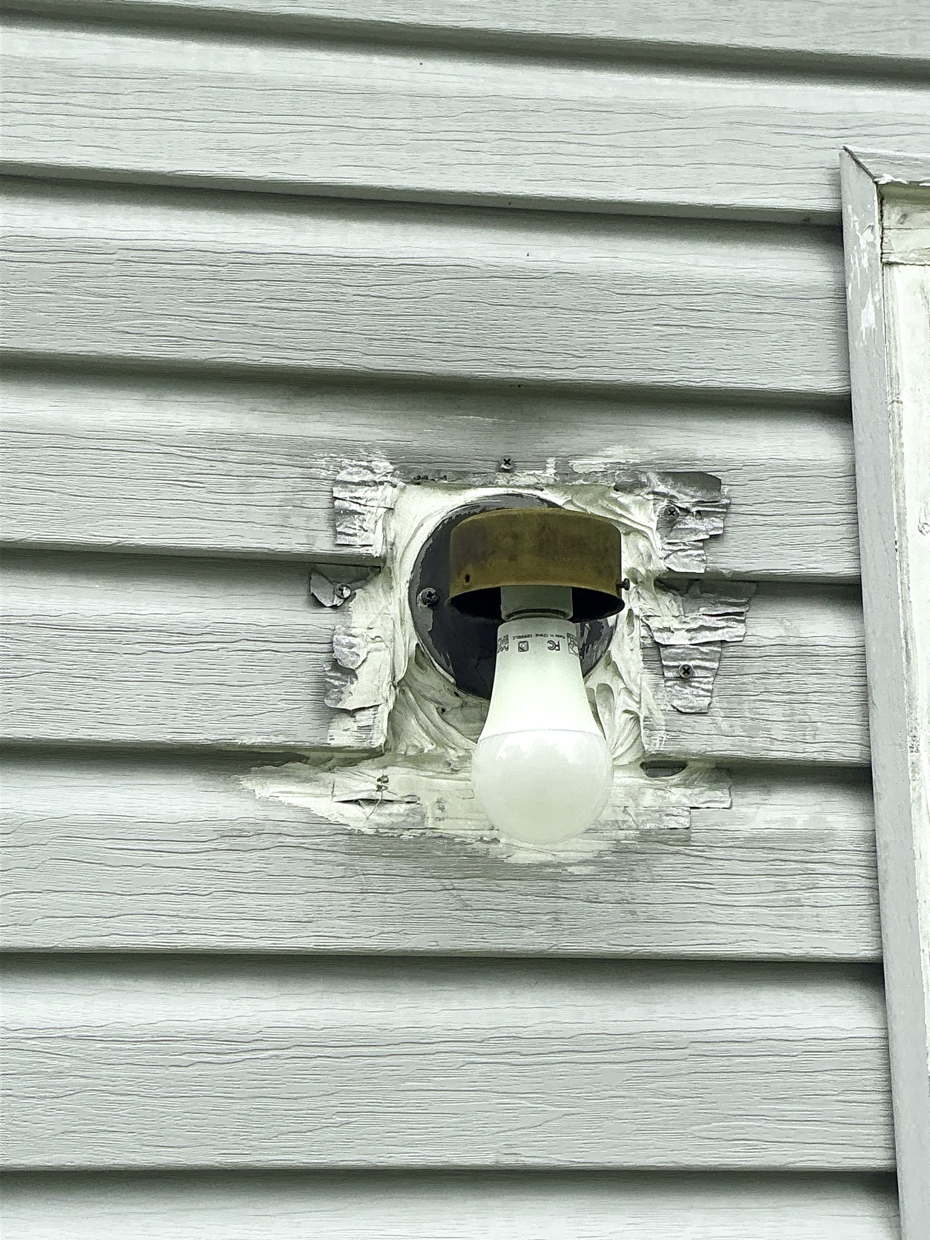 Damaged exterior light fixture mounted on vinyl siding without a globe or fixture cover 2026-07-08