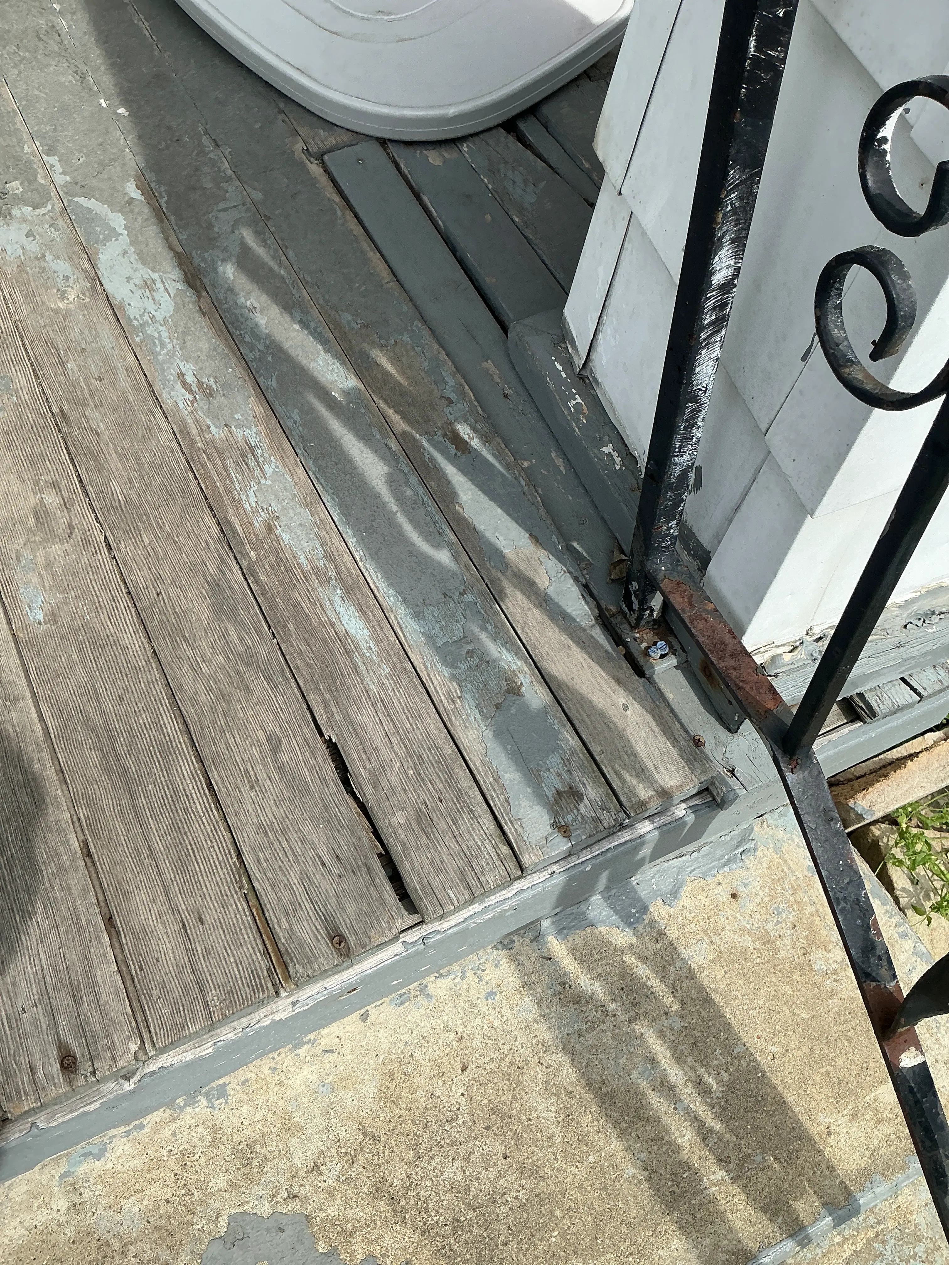 Weathered wooden porch boards with peeling paint and rusted iron handrail base needing repair 2026-07-20