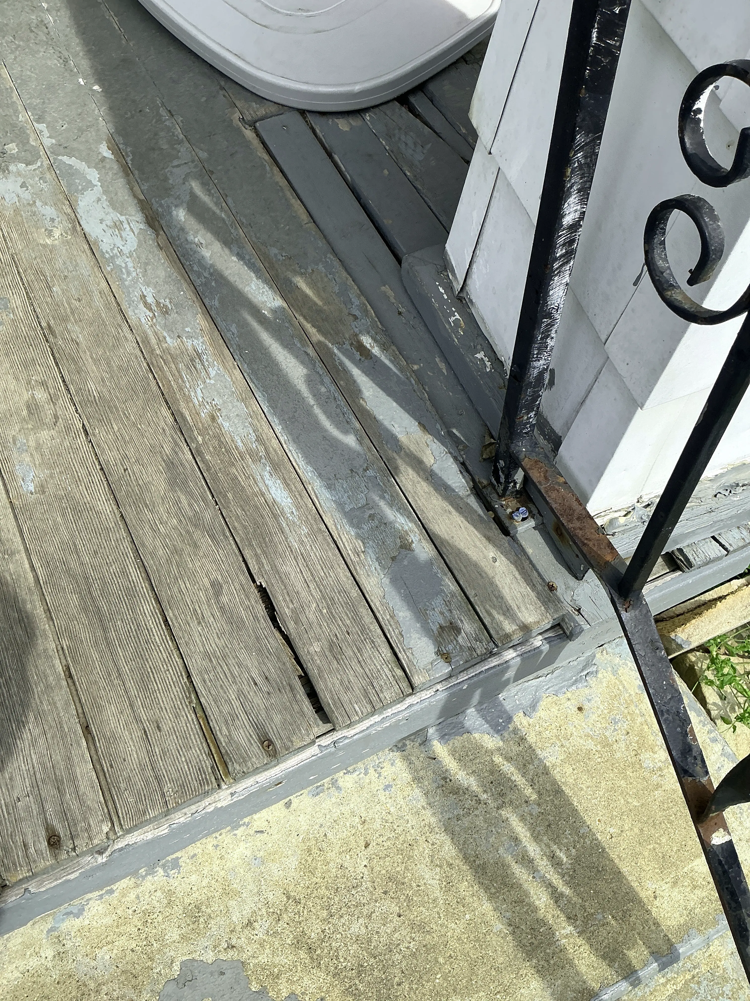 Weathered wooden porch boards with peeling paint and rusted iron handrail base needing repair 2026-07-08