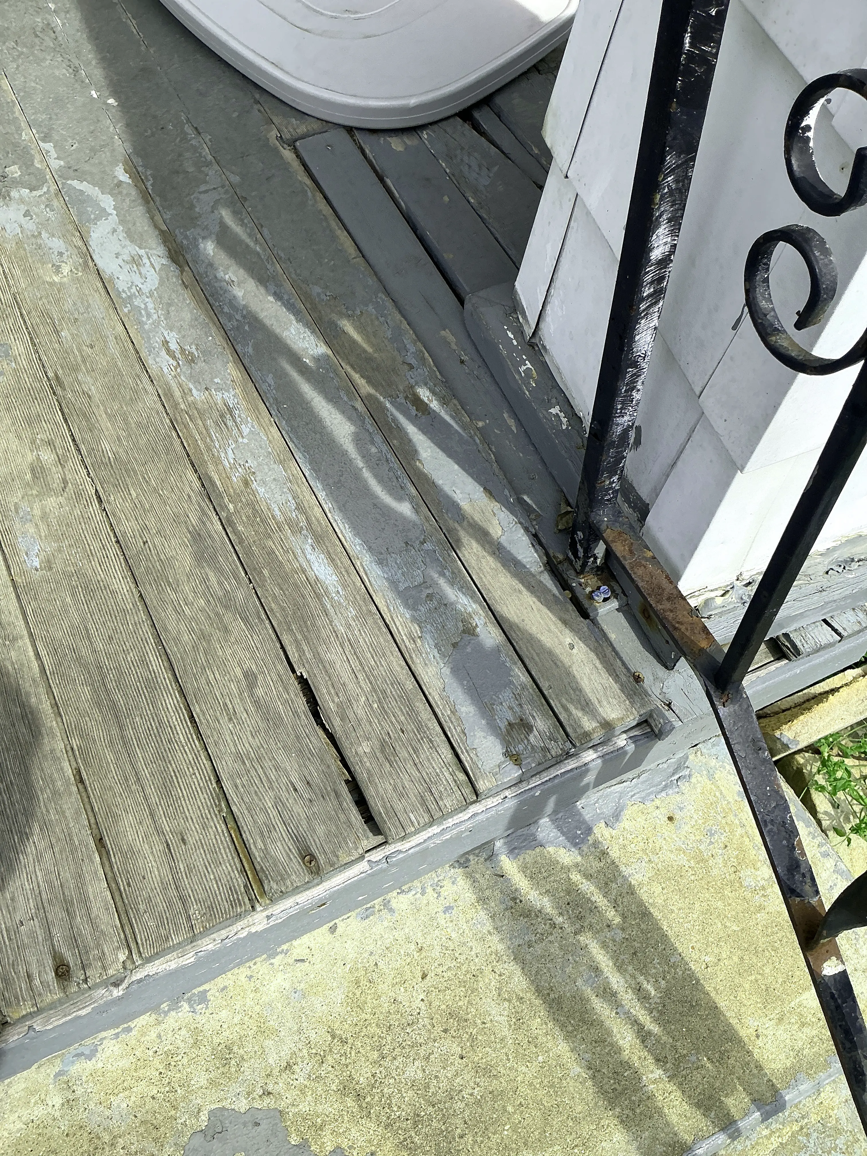 Weathered wooden porch boards with peeling paint and rusted iron handrail base needing repair 2026-07-24