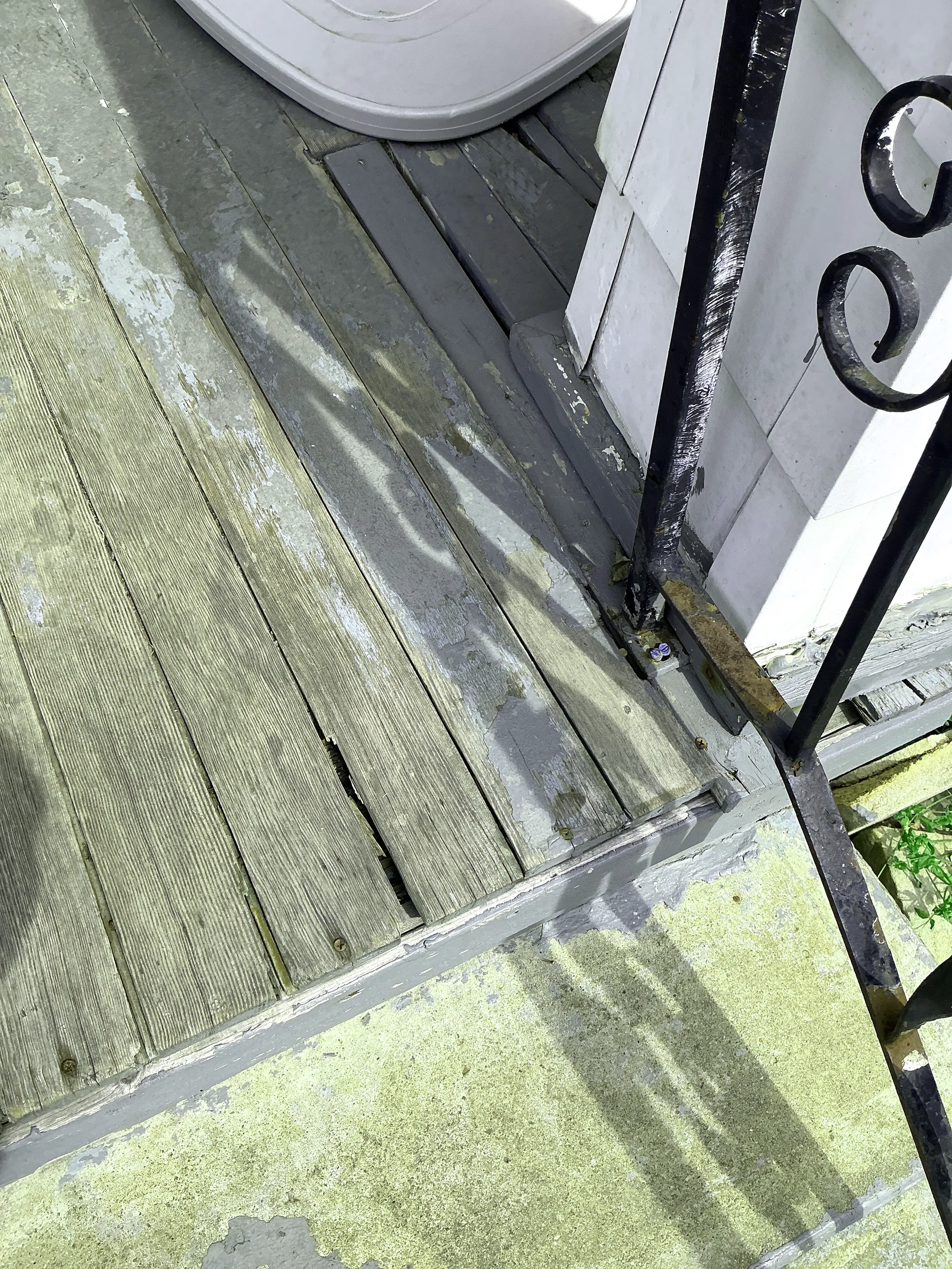 Weathered wooden porch boards with peeling paint and rusted iron handrail base needing repair 2026-07-18