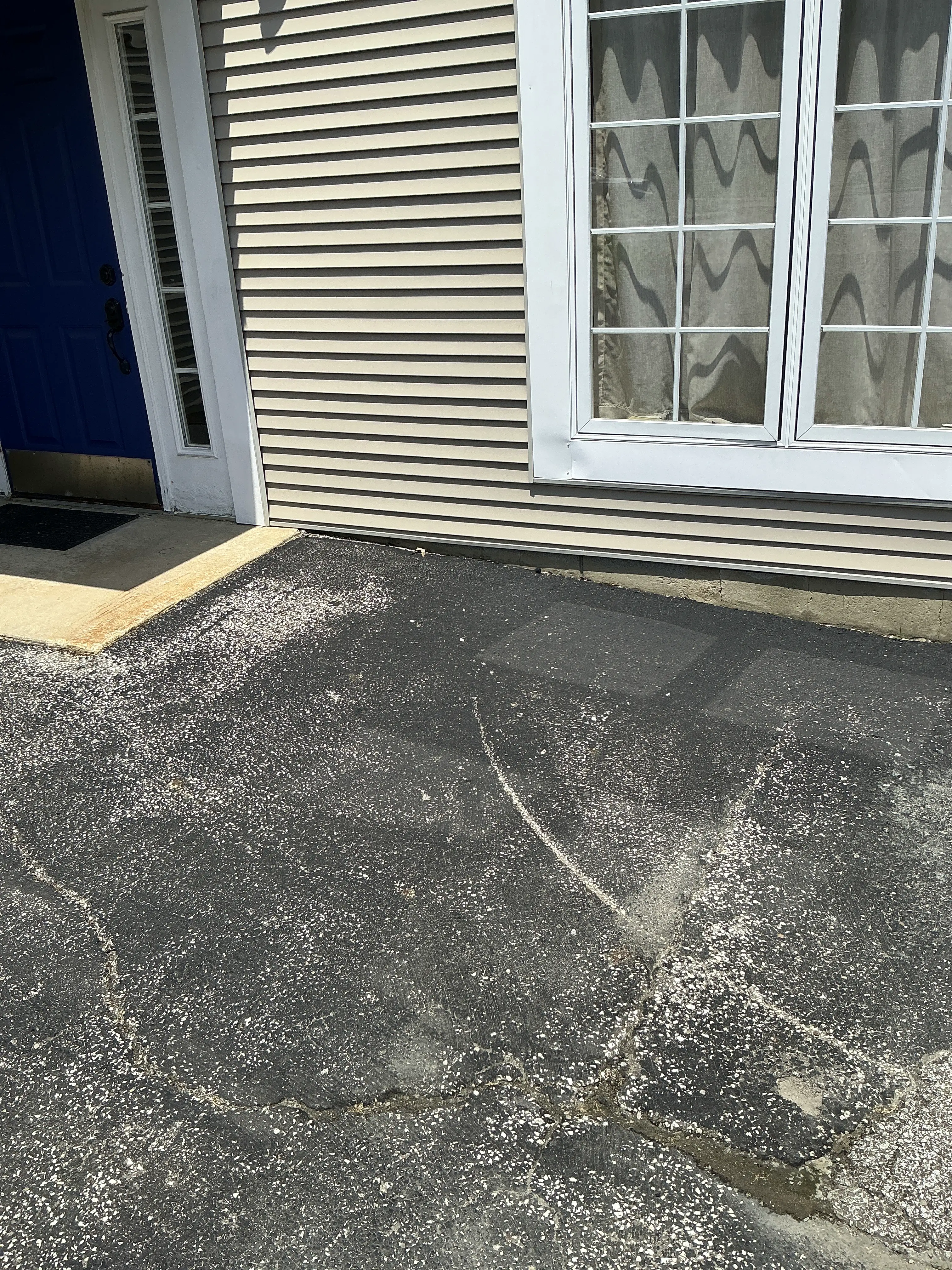 Severe cracking and surface deterioration in asphalt driveway next to home exterior 2026-07-09