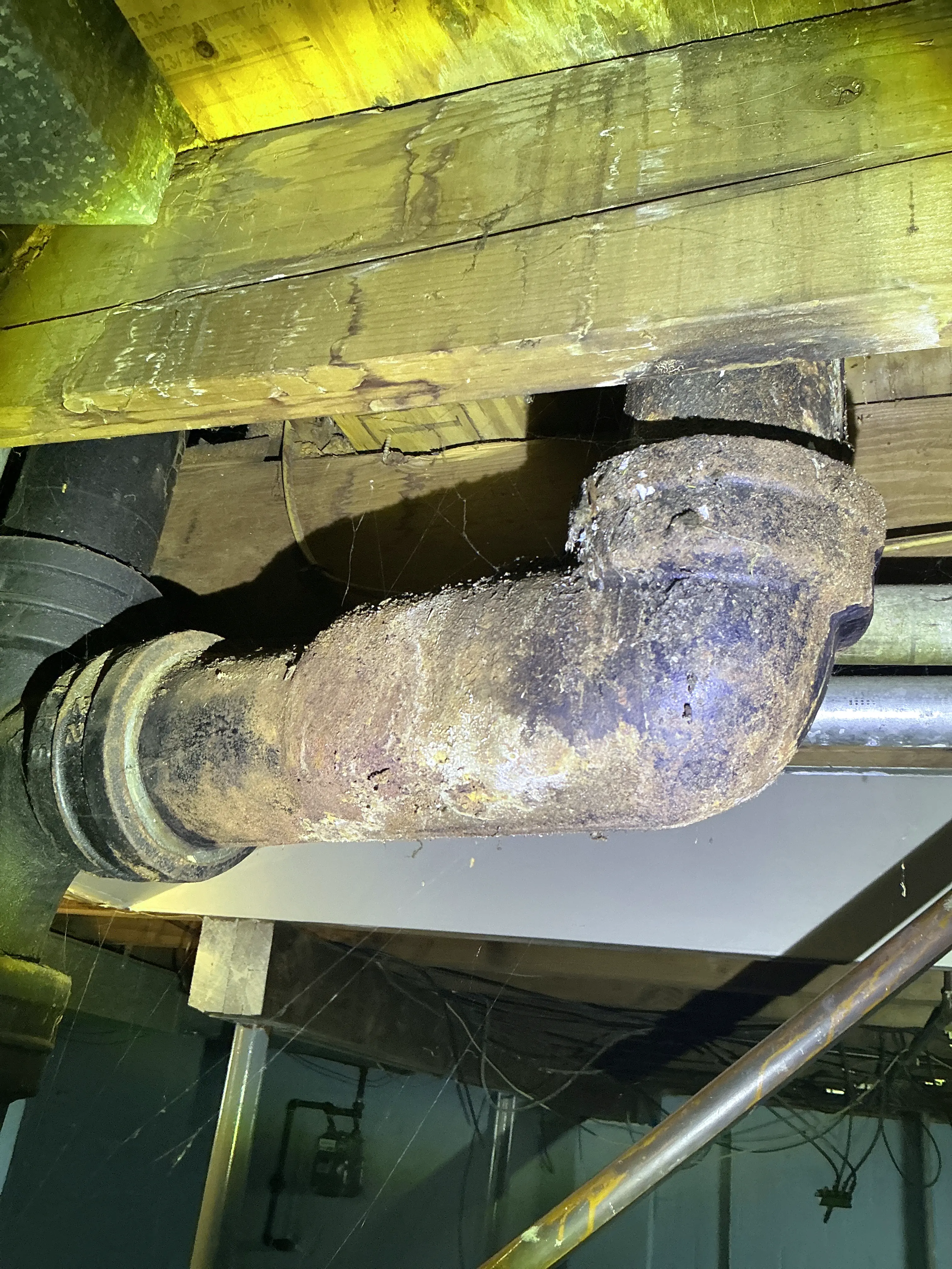 Corroded cast iron plumbing pipe elbow with heavy rust in crawl space framing 2026-07-04