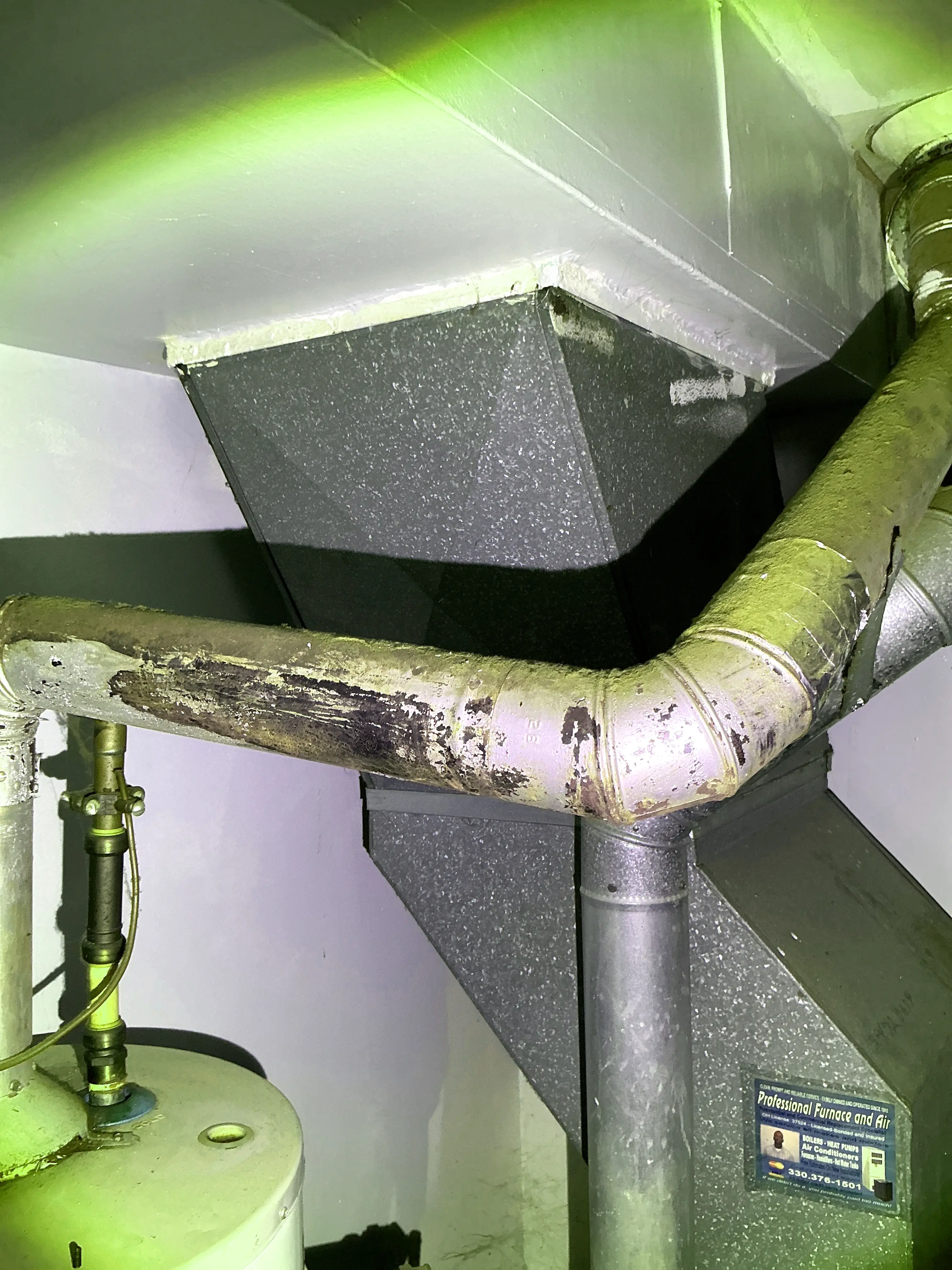 Corroded and discolored metal flue pipe connected to an HVAC duct system in a home basement. 2026-07-15