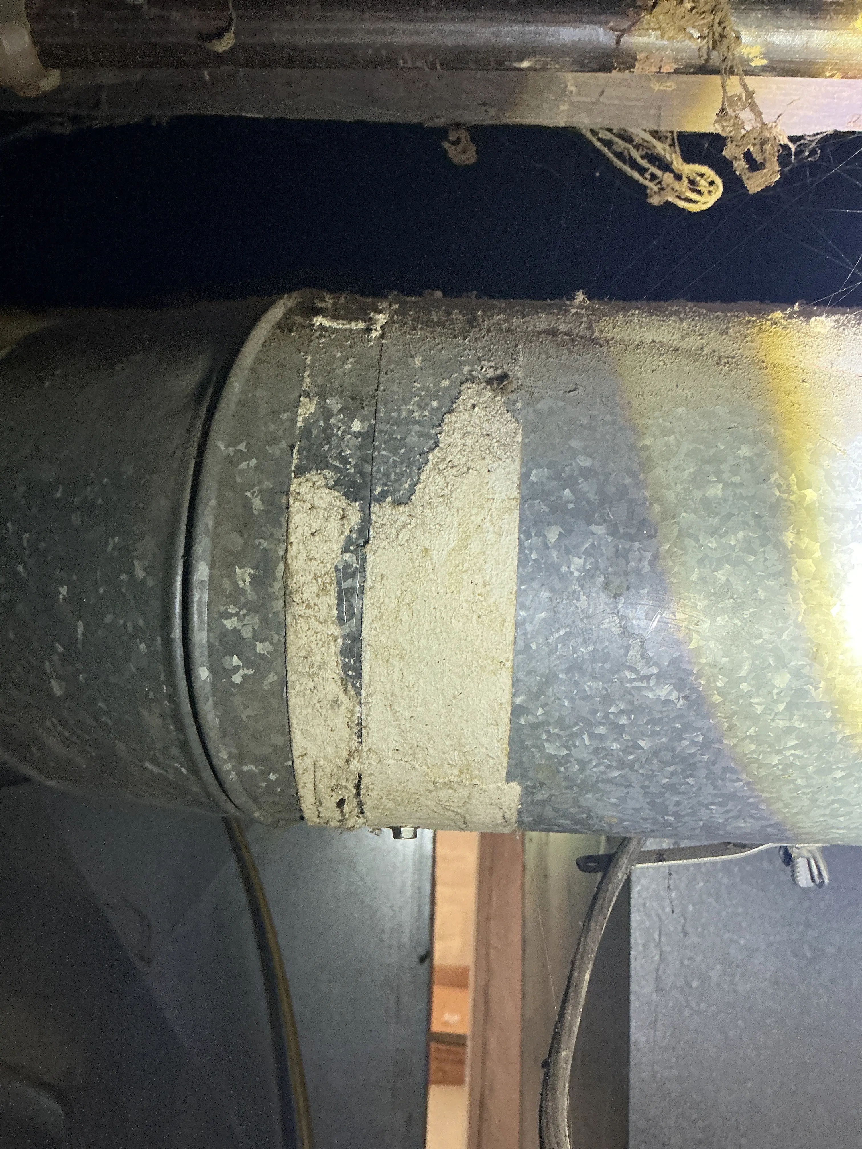 Damaged tape wrap on galvanized metal duct seam in a basement 2026-08-11