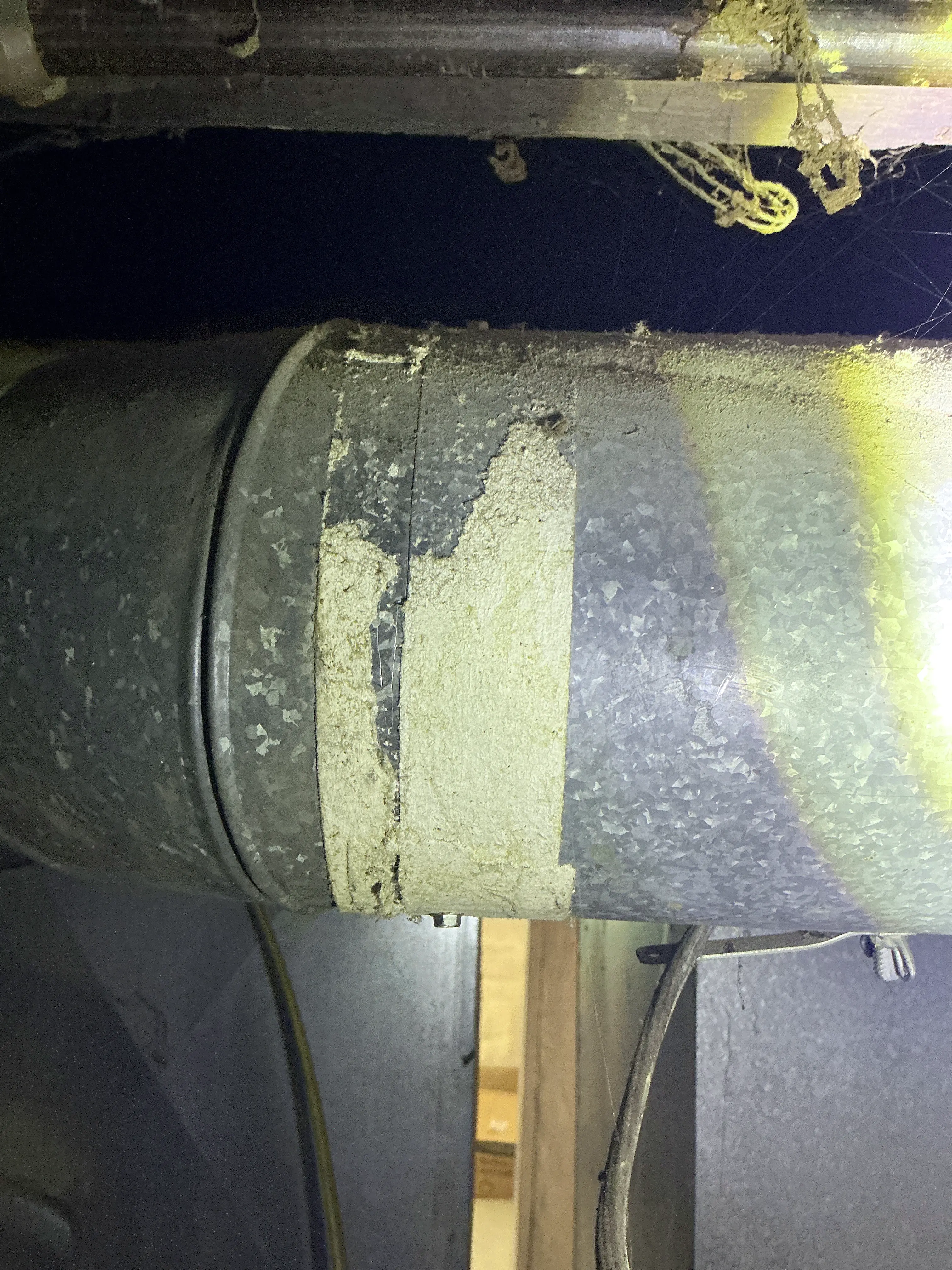 Damaged tape wrap on galvanized metal duct seam in a basement 2026-08-23