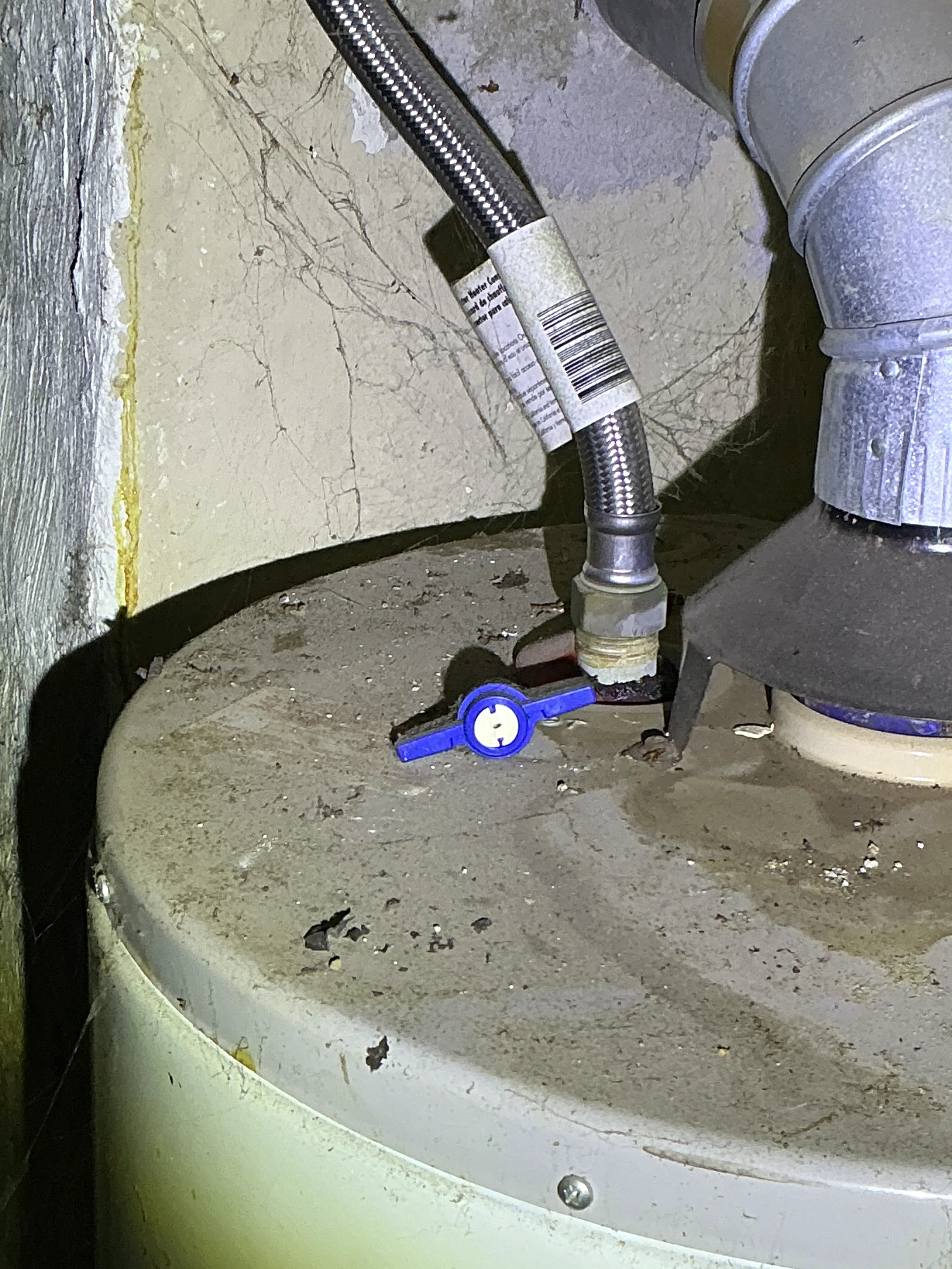 Gas shut-off valve with a blue handle connected to a flexible line on a water heater showing corrosion. 2026-07-04