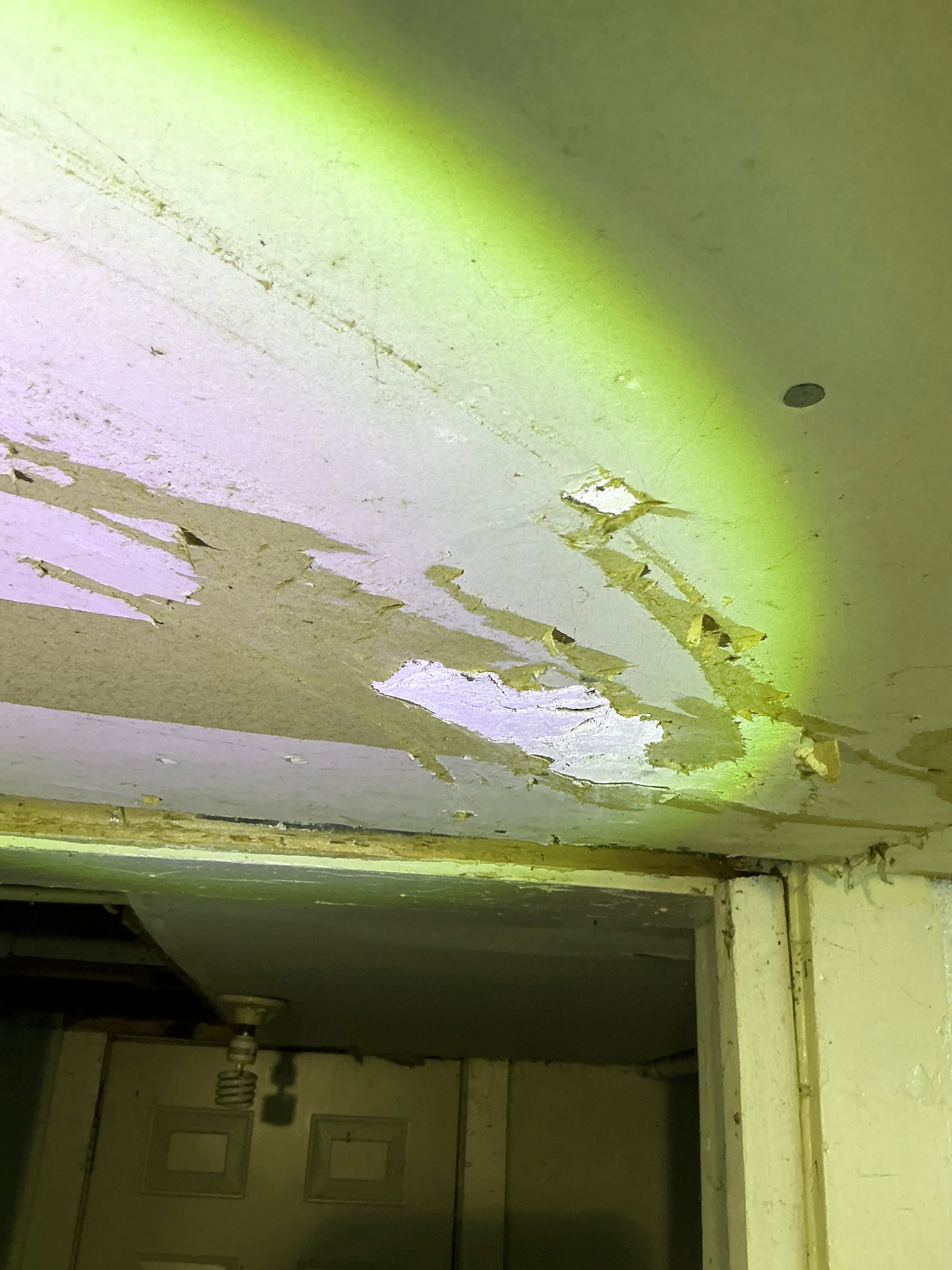 Close-up of damaged interior drywall with torn paper facing illuminated by flashlight during home inspection 2026-07-08