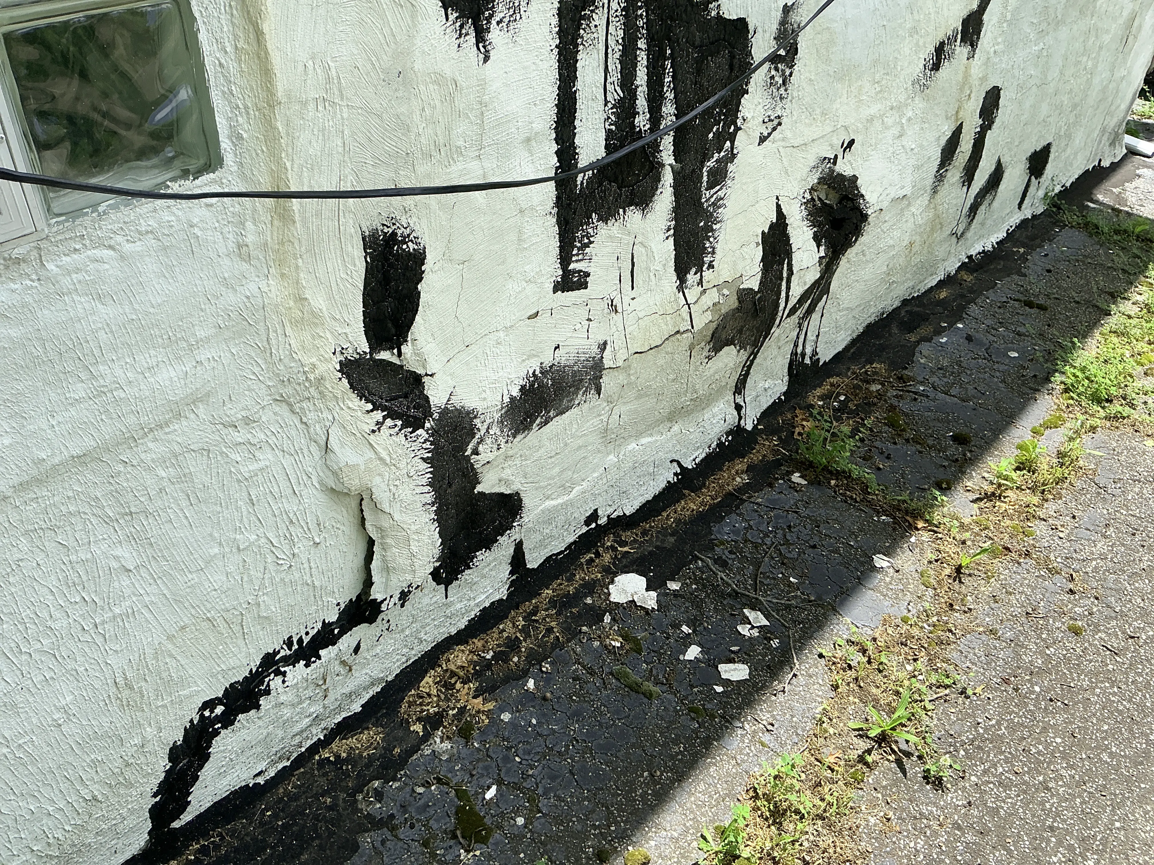 Cracked and bulging exterior stucco wall with crude sealant patches near ground level 2026-08-30