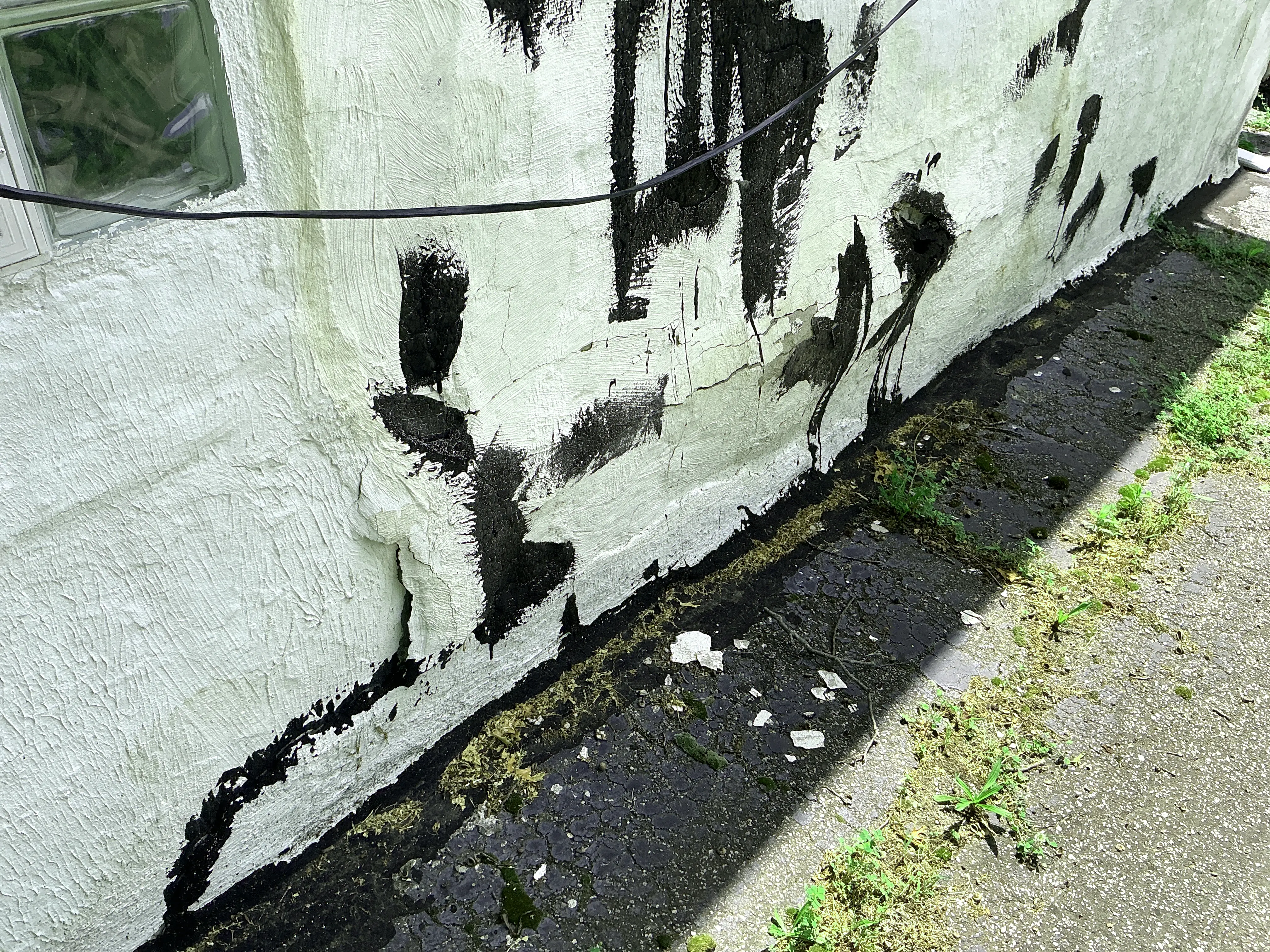 Cracked and bulging exterior stucco wall with crude sealant patches near ground level 2026-07-27