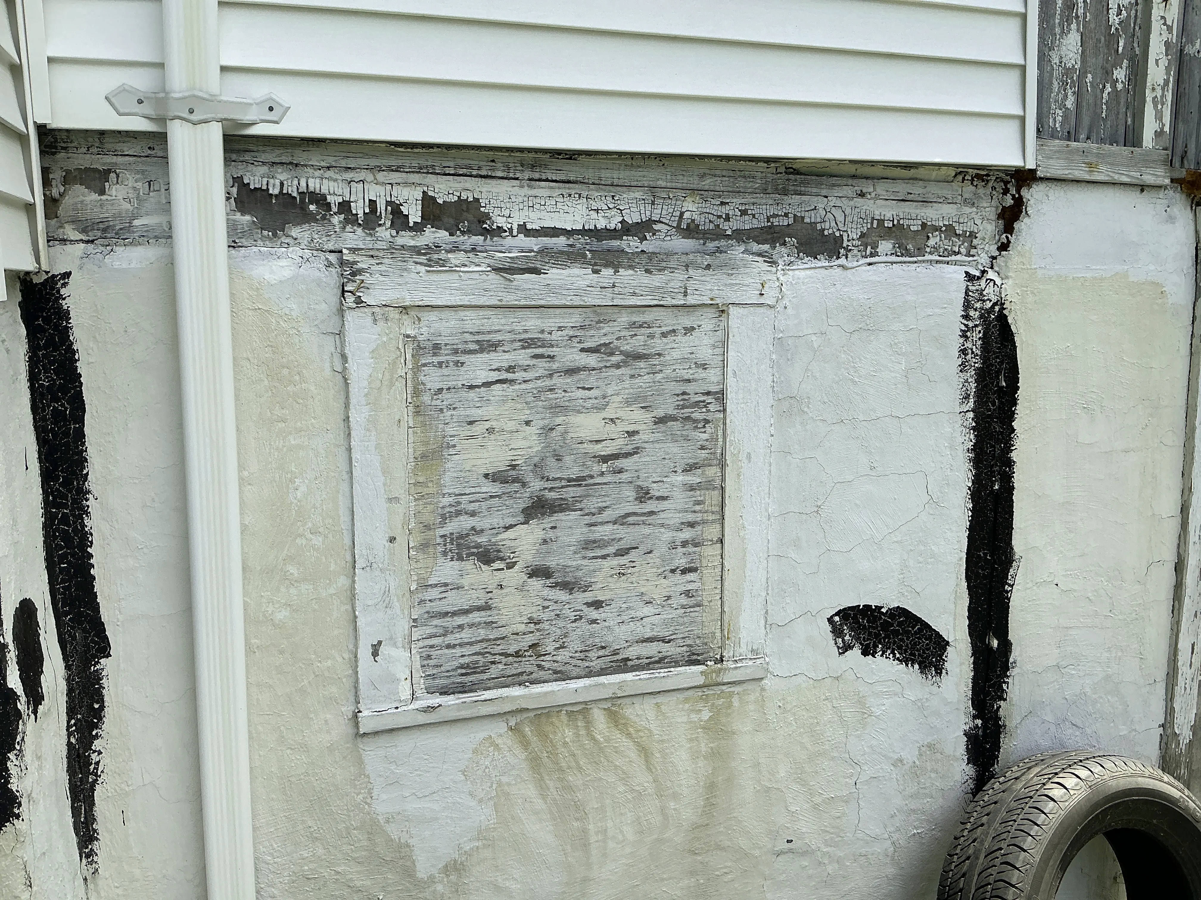 Deteriorated foundation wall with peeling paint and boarded window during home inspection 2026-07-24