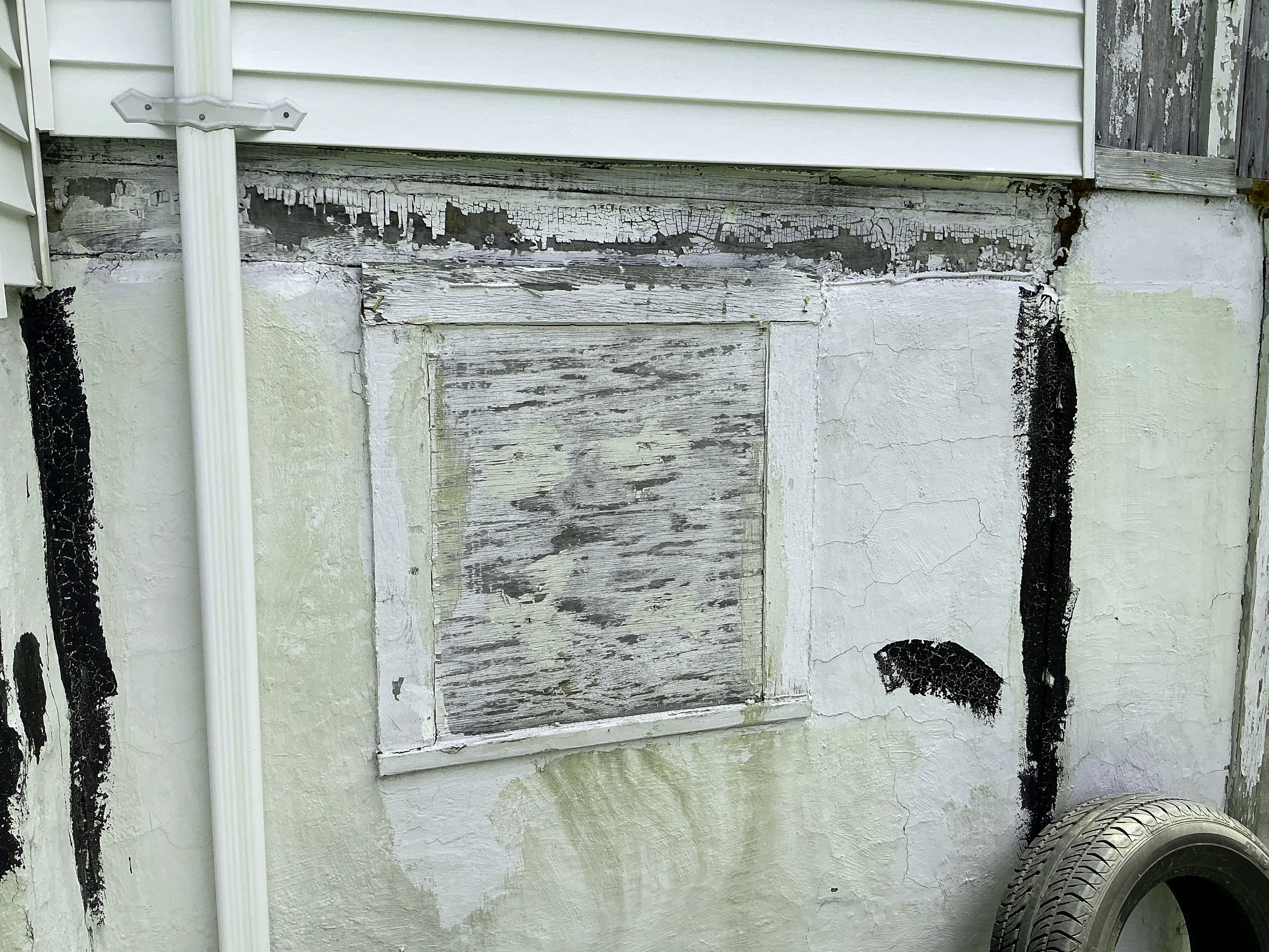 Deteriorated foundation wall with peeling paint and boarded window during mold inspection 2026-07-09