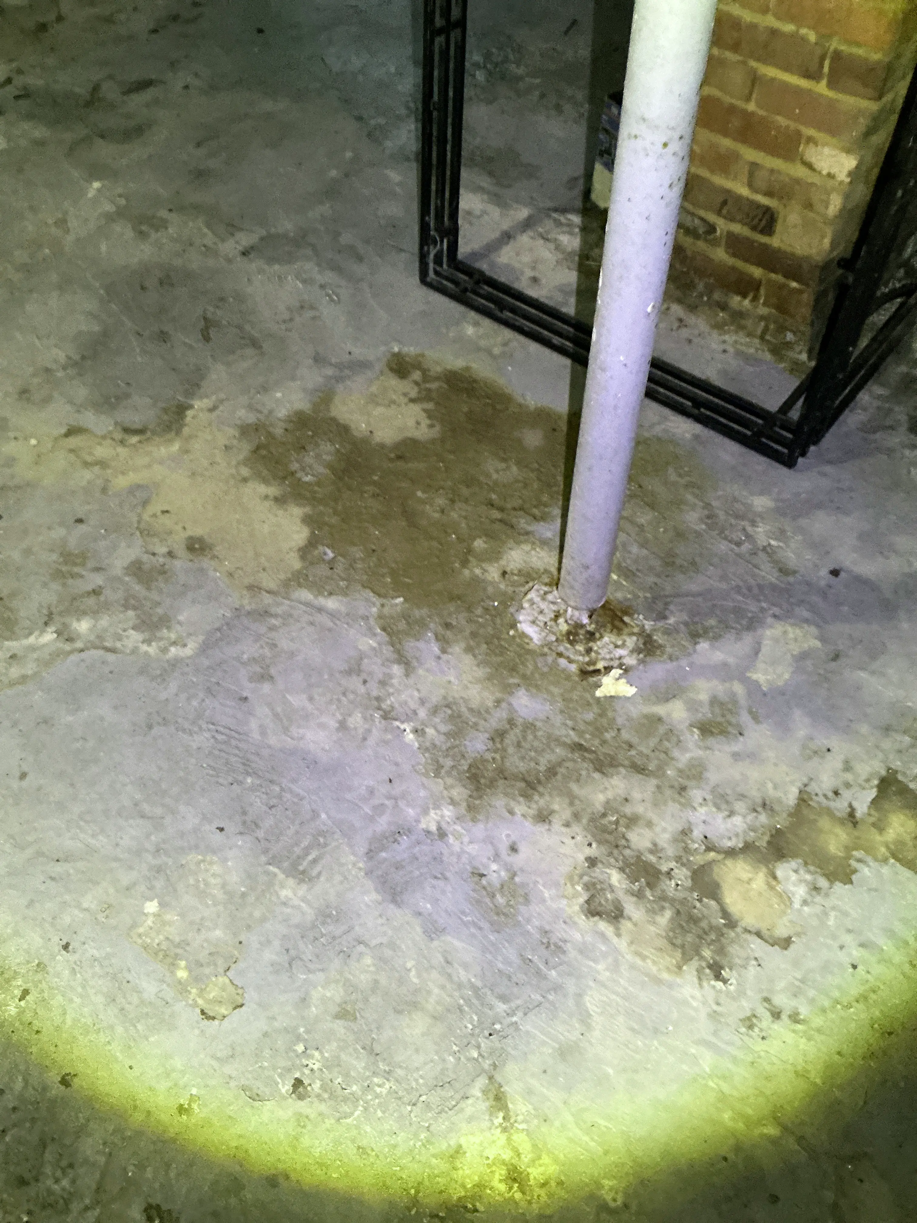 Water staining and moisture buildup around a pipe penetration in a basement concrete floor during a mold testing. 2026-08-29