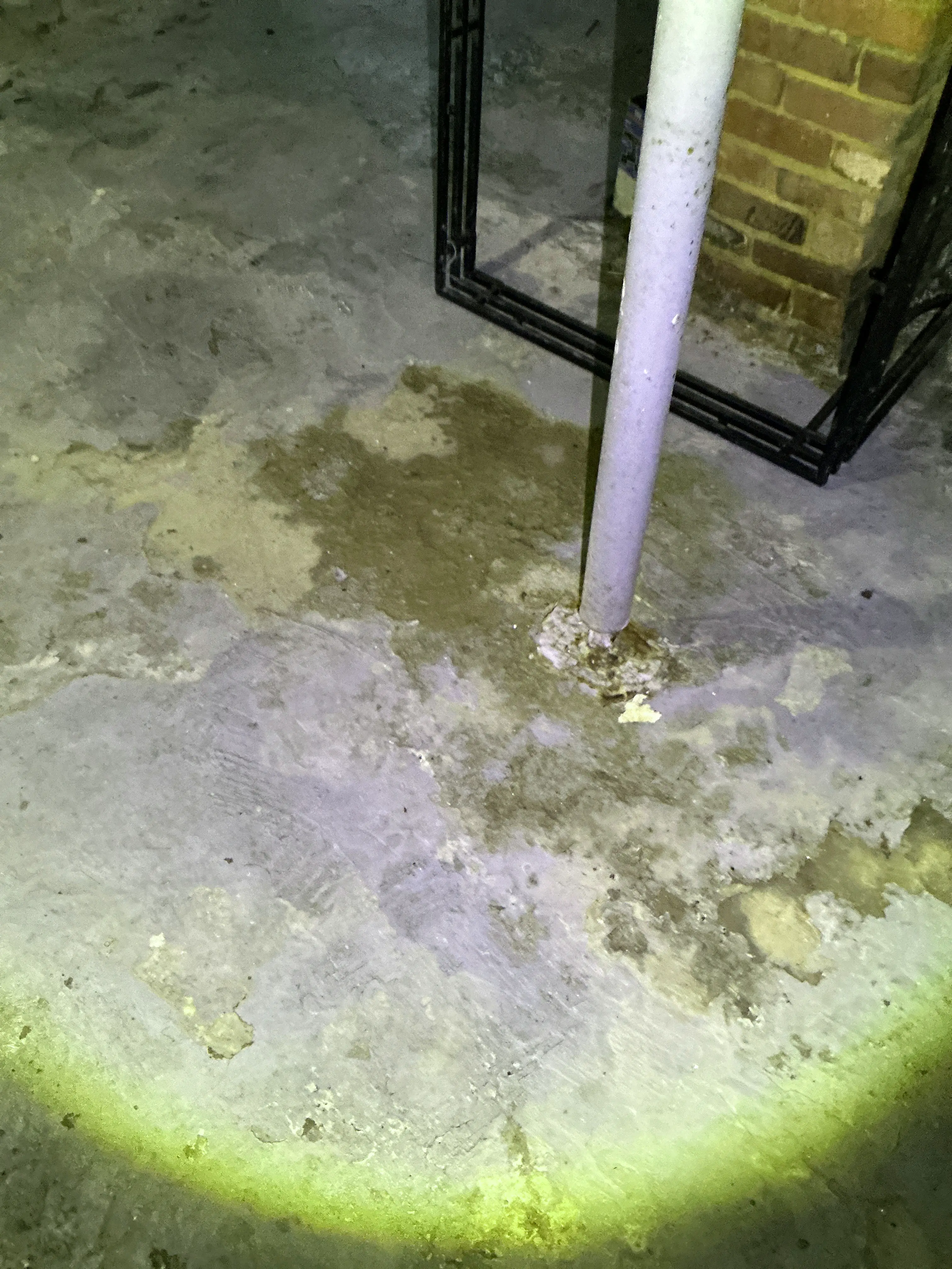 Water staining and moisture buildup around a pipe penetration in a basement concrete floor during a home inspection. 2026-08-21