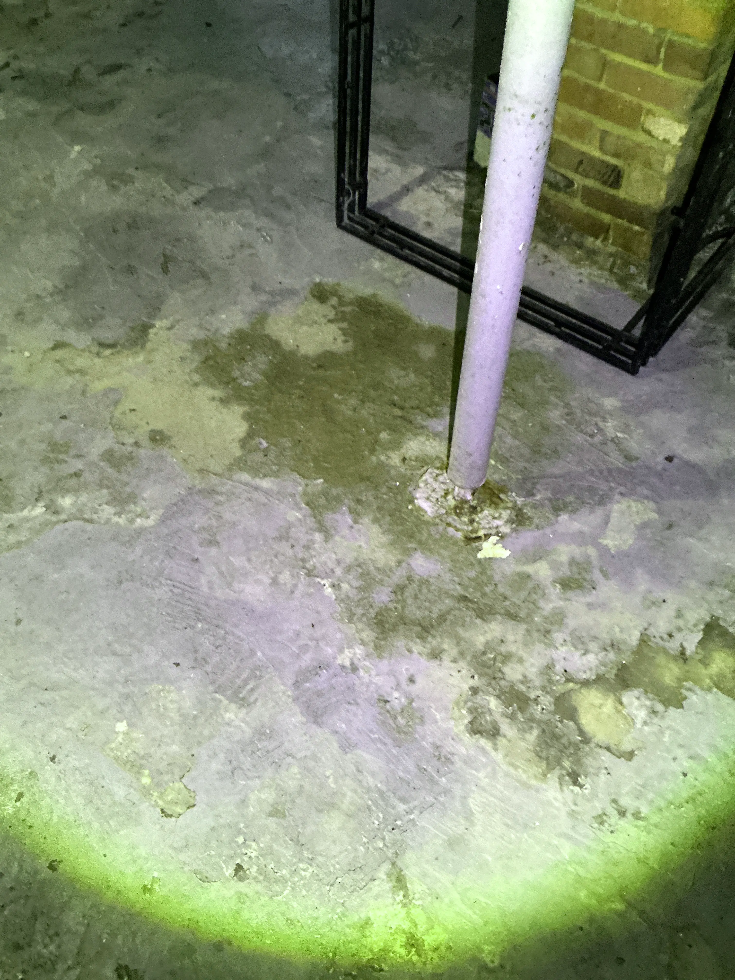 Water staining and moisture buildup around a pipe penetration in a basement concrete floor during a home inspection. 2026-08-16