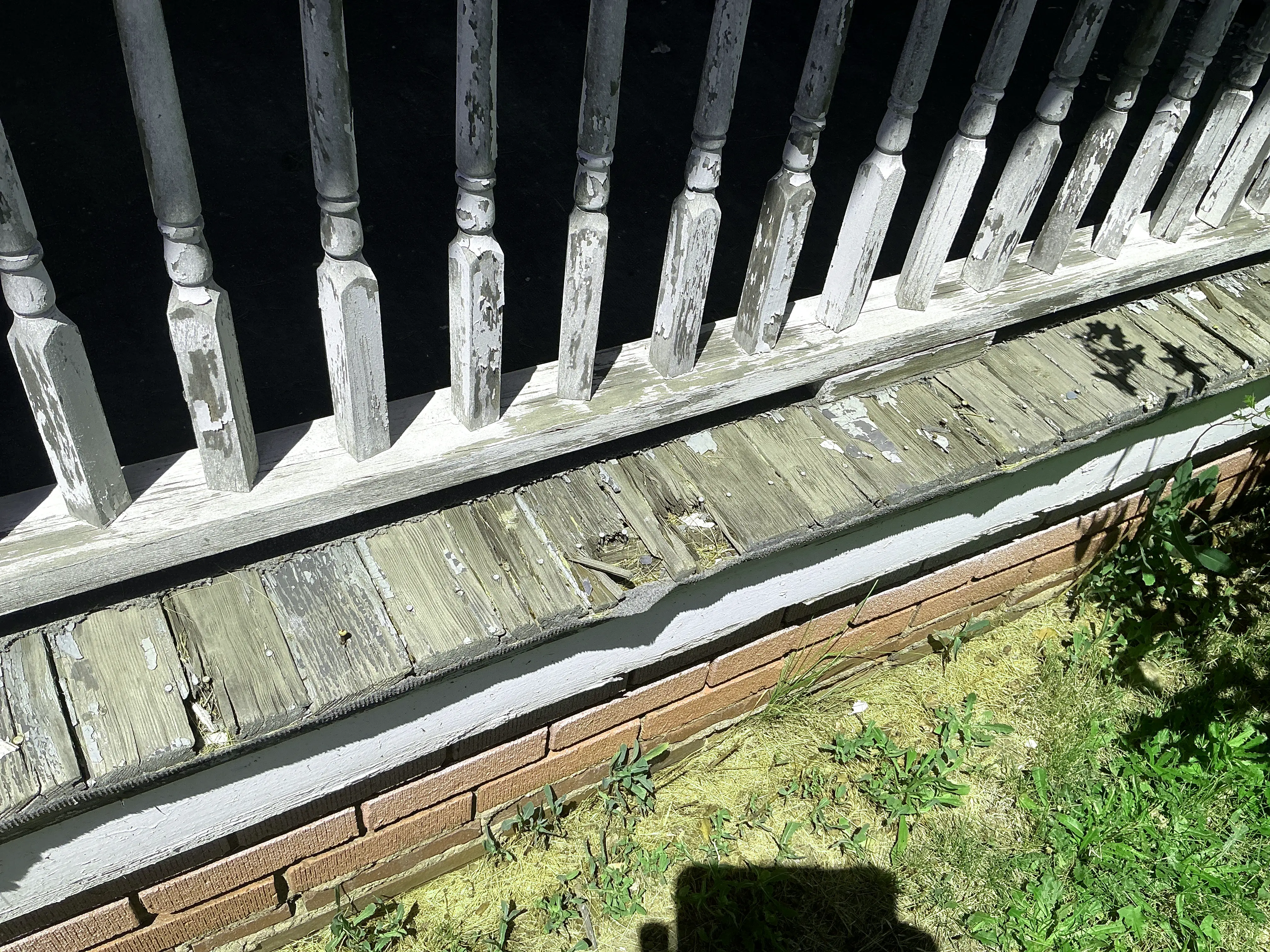Weathered wood rot and peeling paint on porch floorboards below railing balusters 2026-08-30