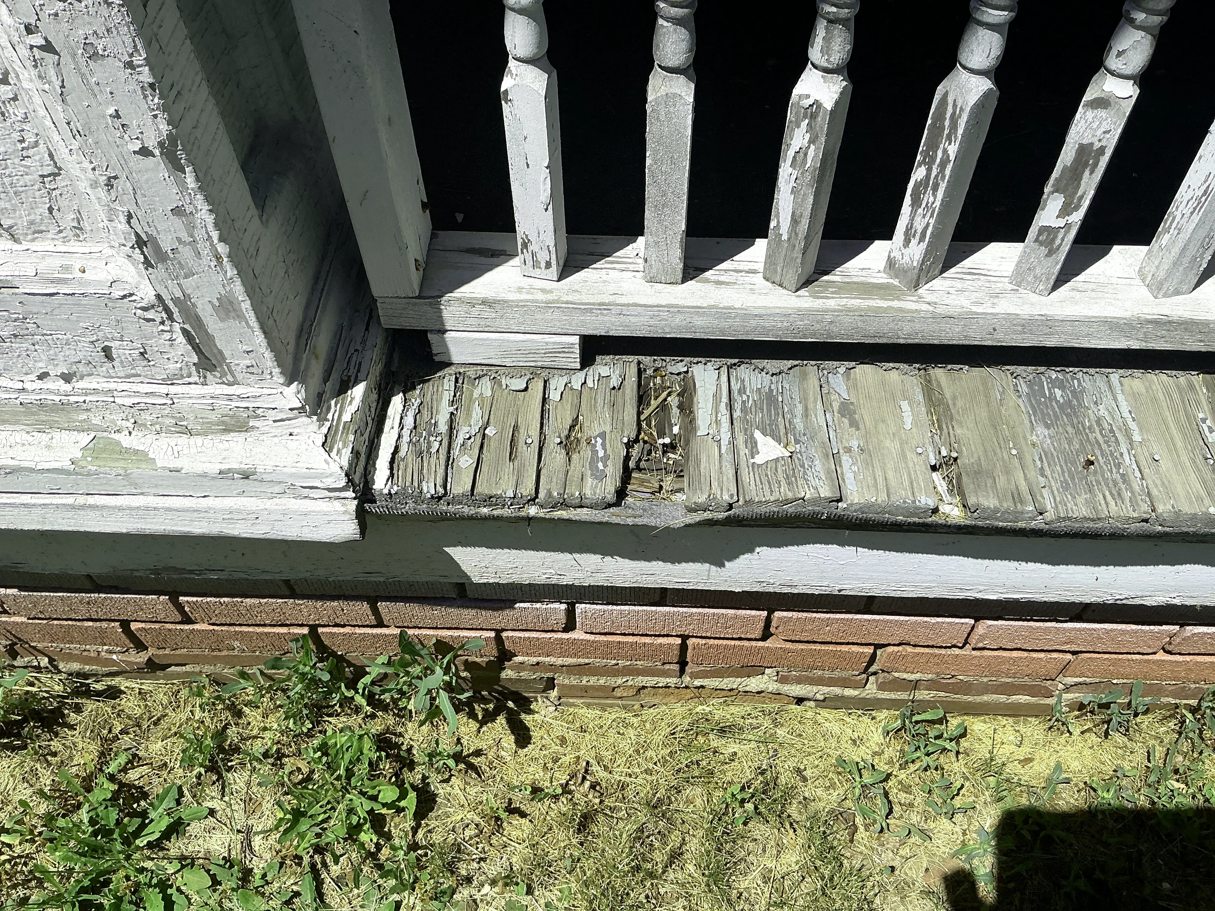 Rotting wooden porch decking with peeling paint under porch balusters 2026-08-10