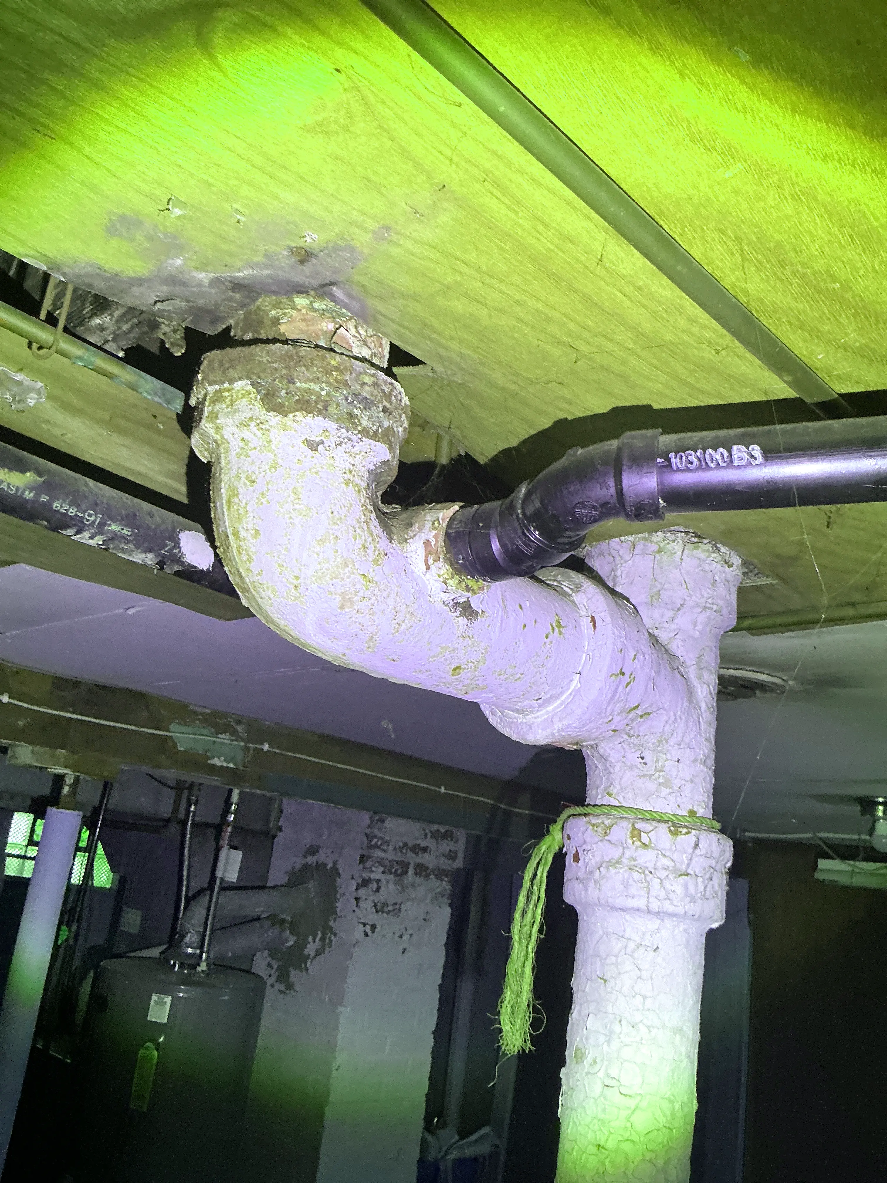 Corroded cast iron drain line with ABS plastic pipe connection in basement ceiling 2026-08-10