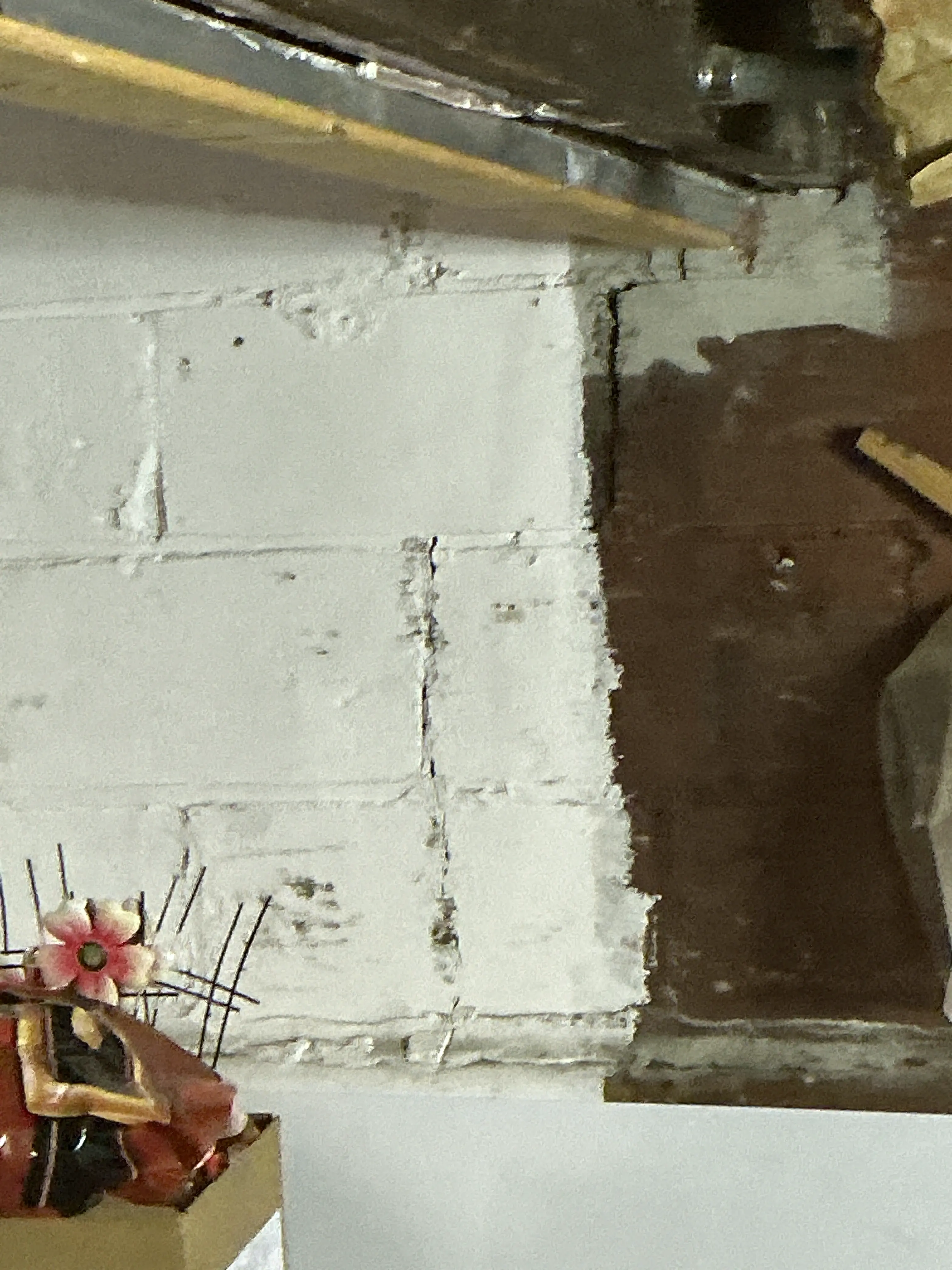 Damaged wall surface with exposed mortar and cracked plaster behind kitchen cabinet. 2026-08-24
