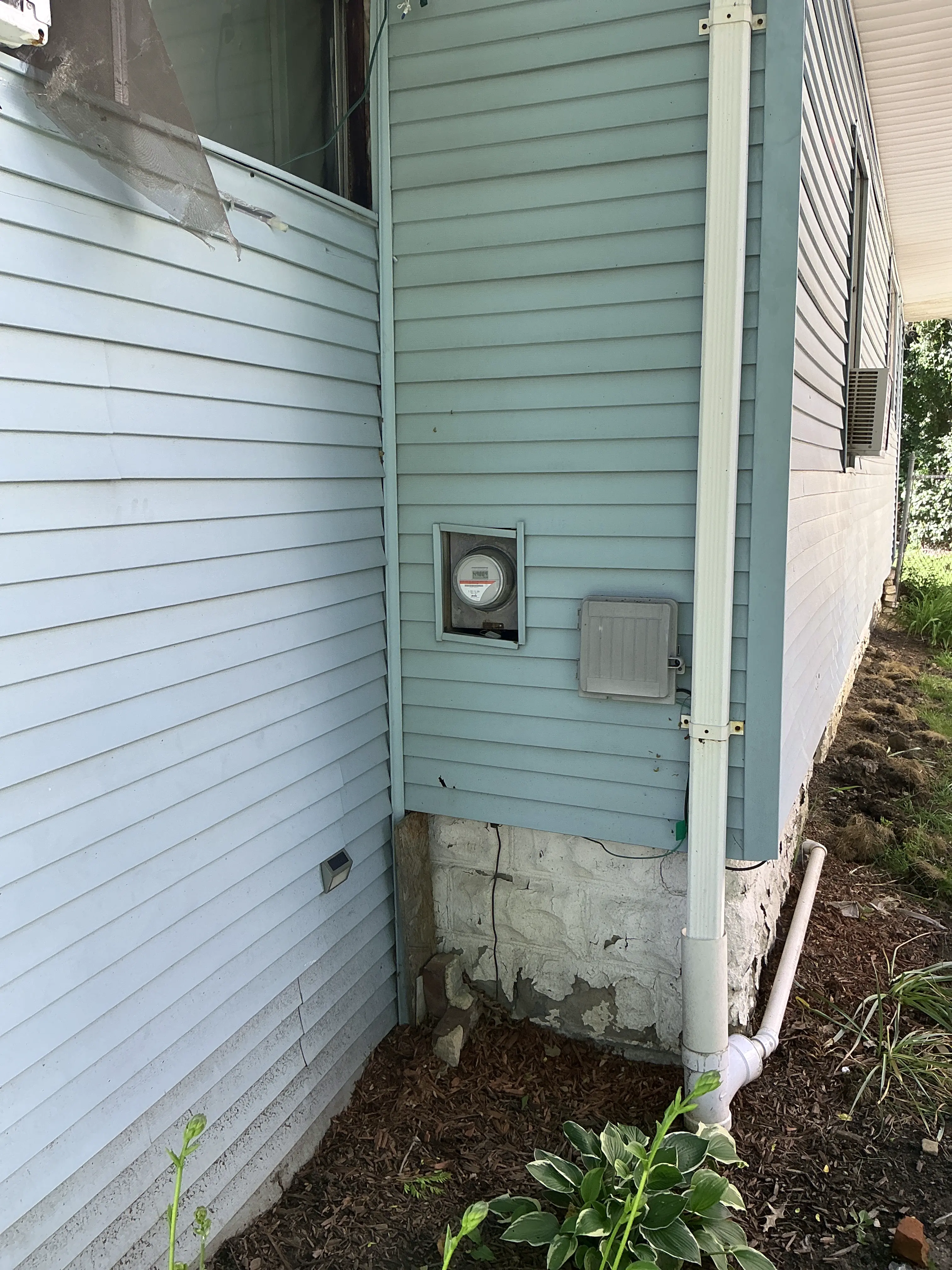 Deteriorated foundation parging coat along exterior home wall and garden bed. 2026-08-19