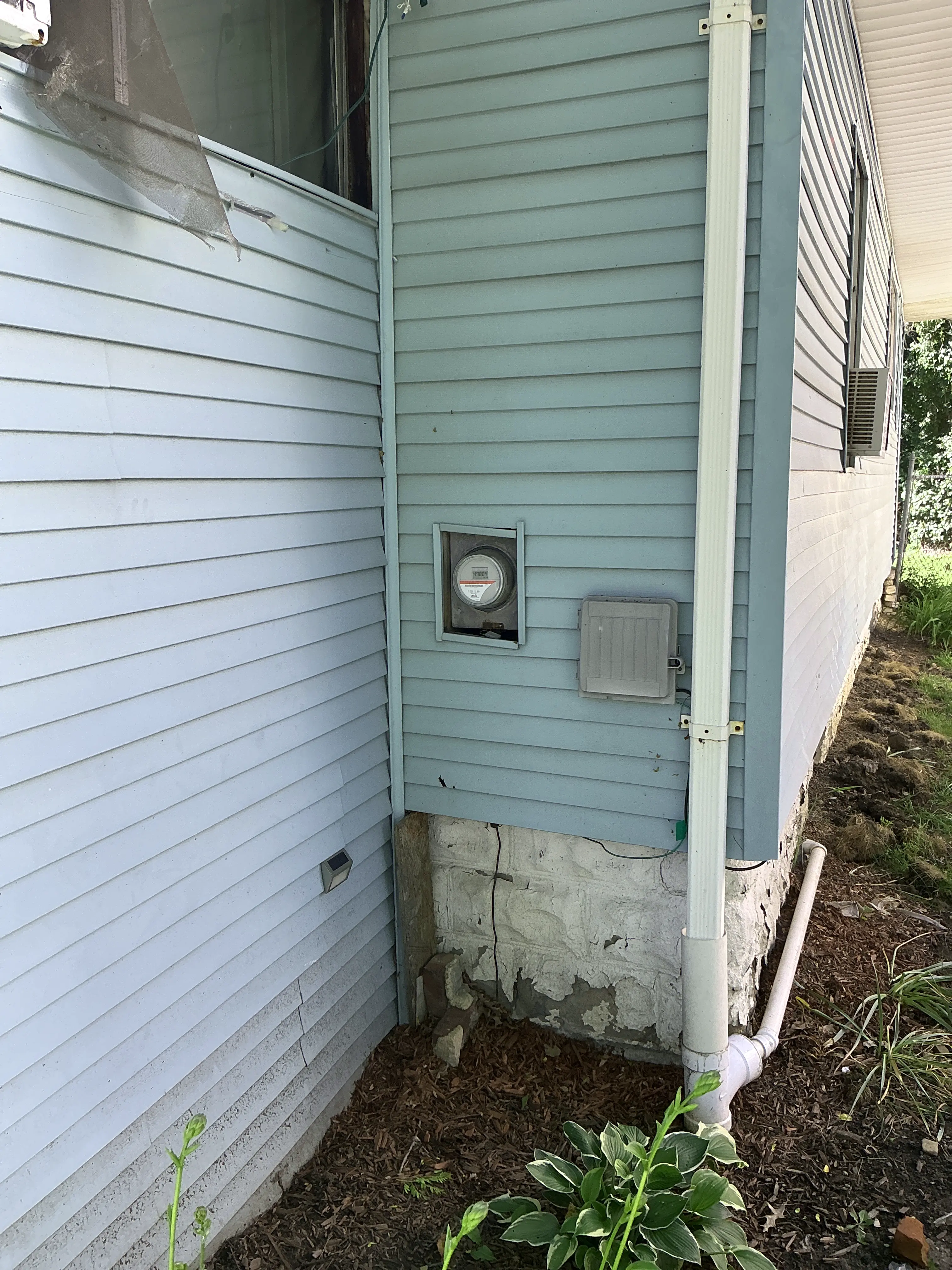 Deteriorated foundation parging coat along exterior home wall and garden bed. 2026-08-09