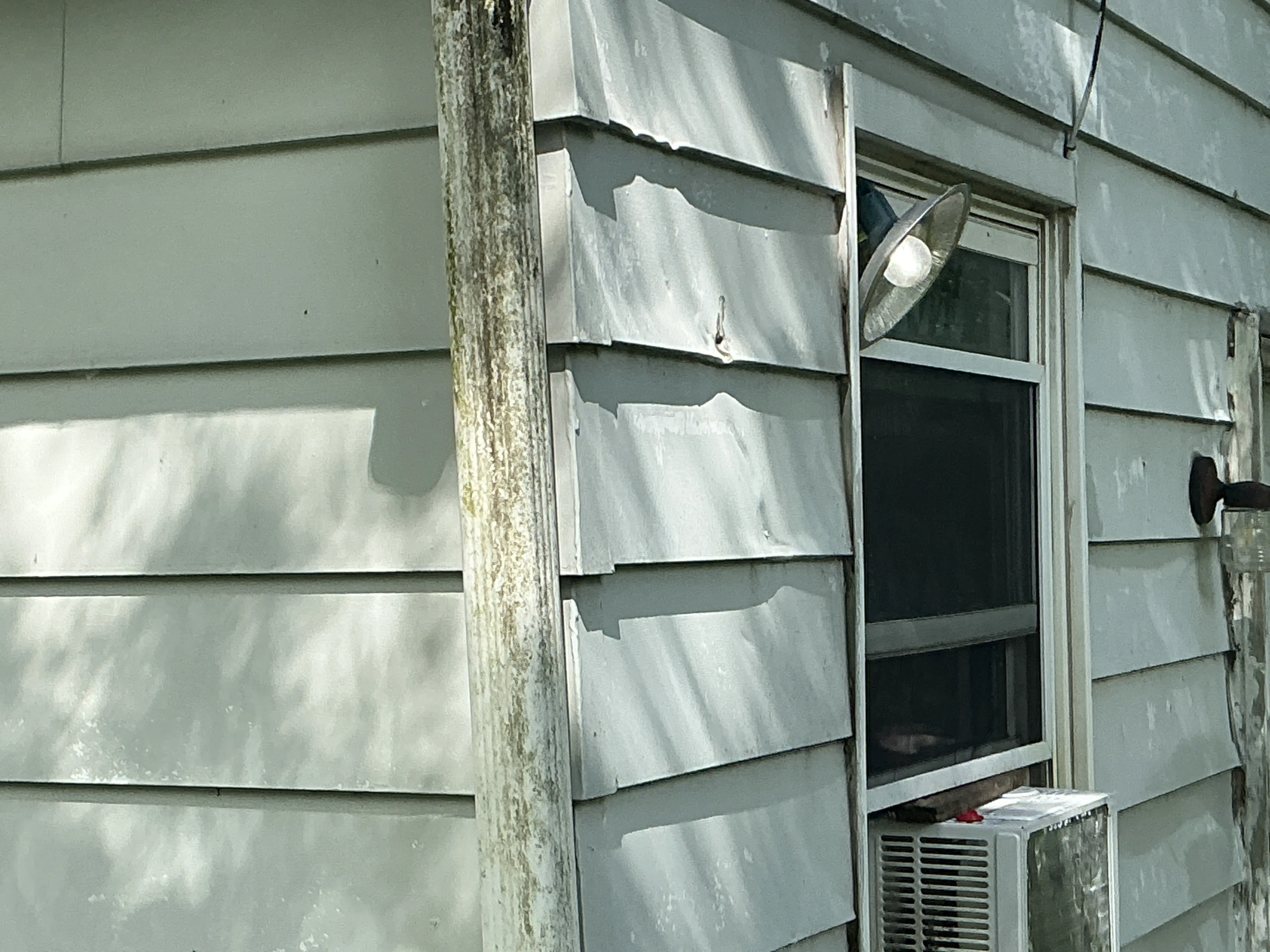 Dented metal siding and weathered downspout on exterior wall of home 2026-08-05