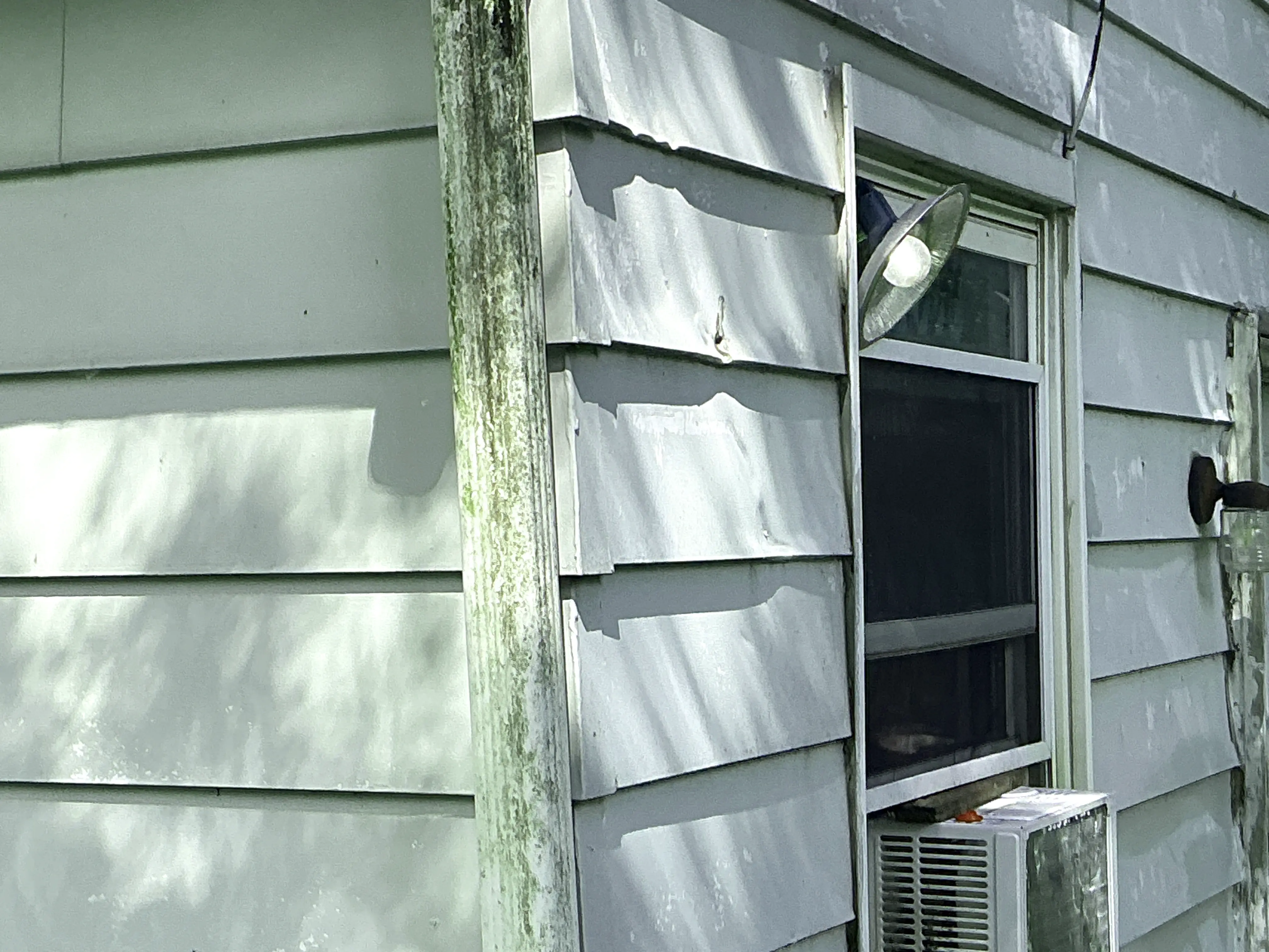 Dented metal siding and weathered downspout on exterior wall of home 2026-07-09