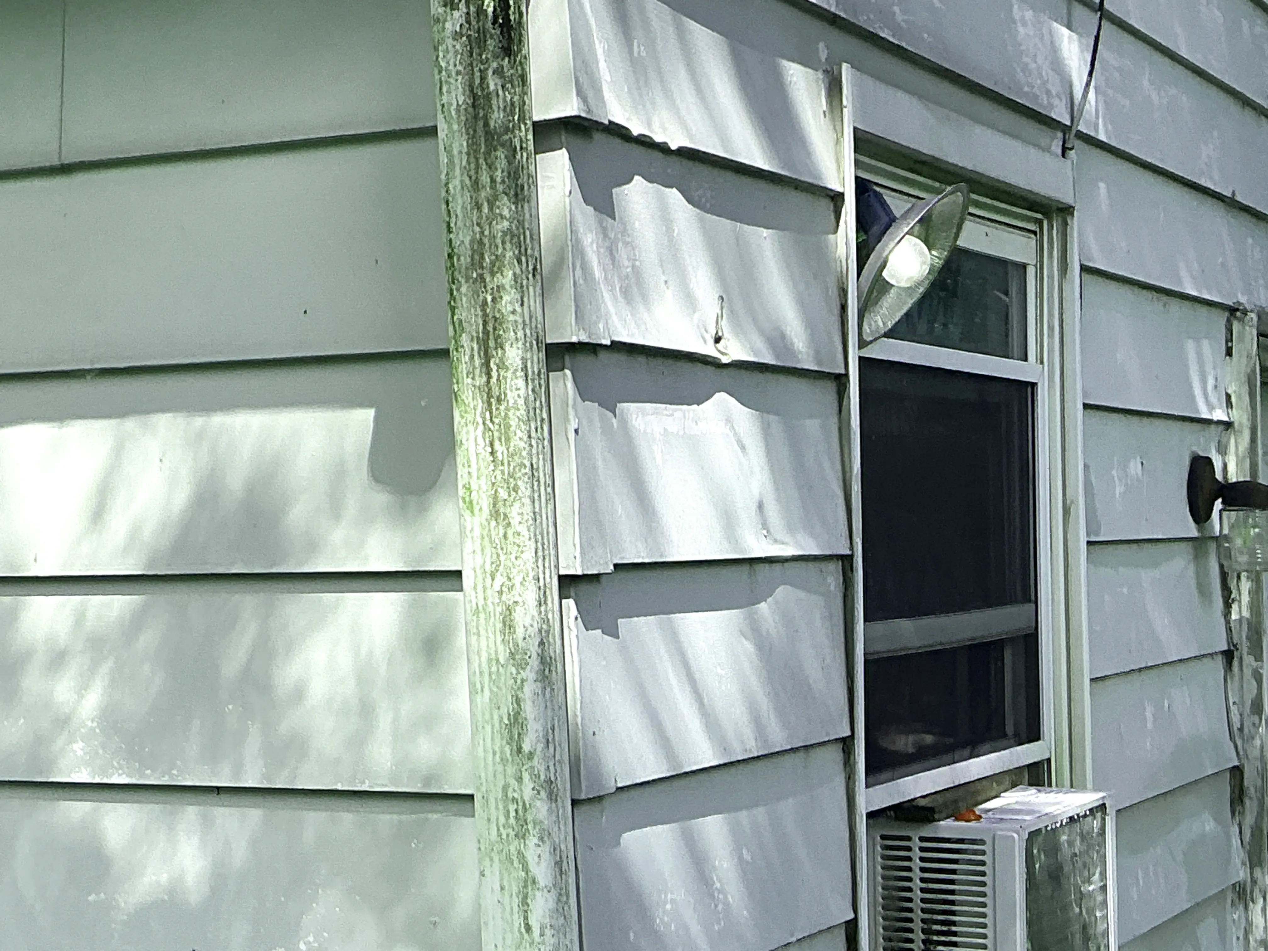 Dented metal siding and weathered downspout on exterior wall of home 2026-08-16