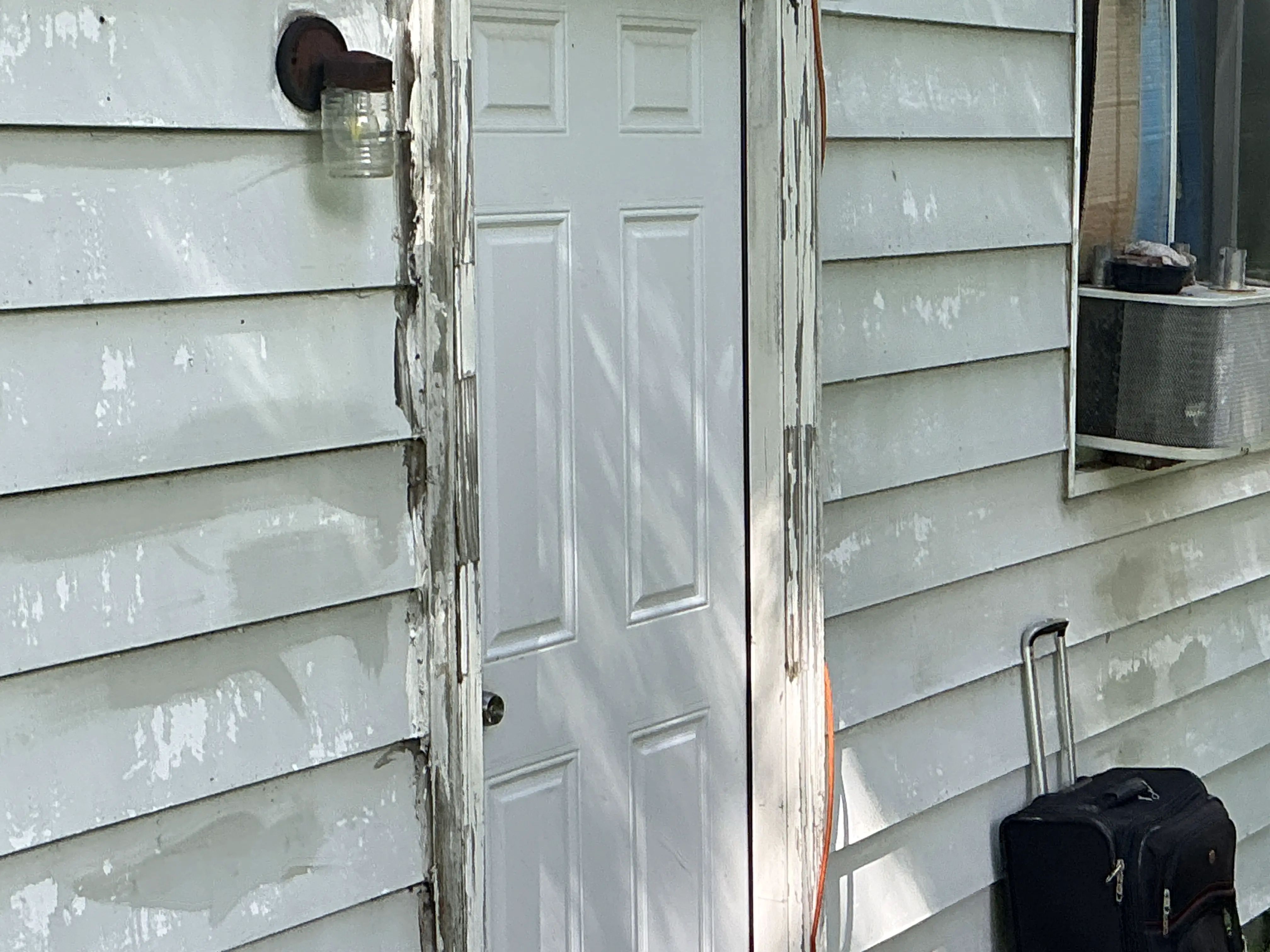 Peeling paint and weathered wood trim around an exterior door on house siding 2026-08-28