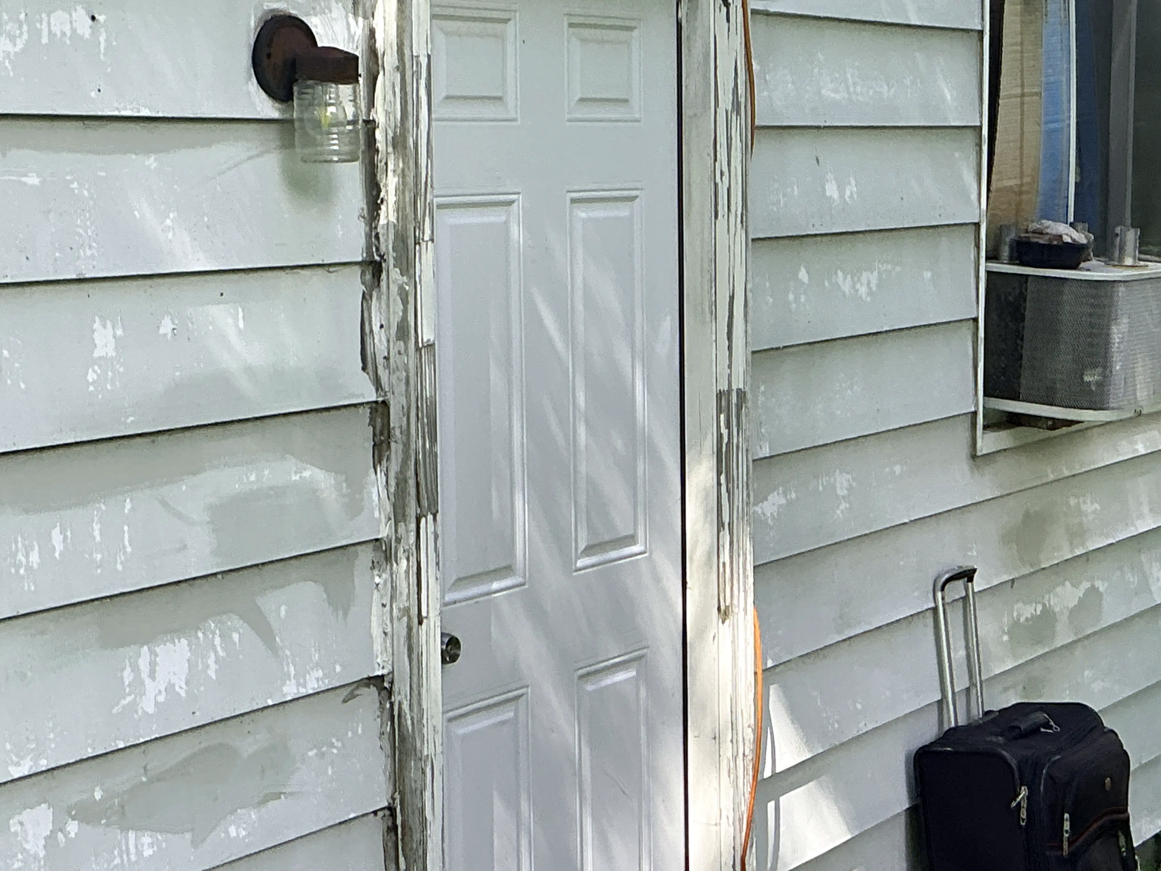 Peeling paint and weathered wood trim around an exterior door on house siding 2026-08-13