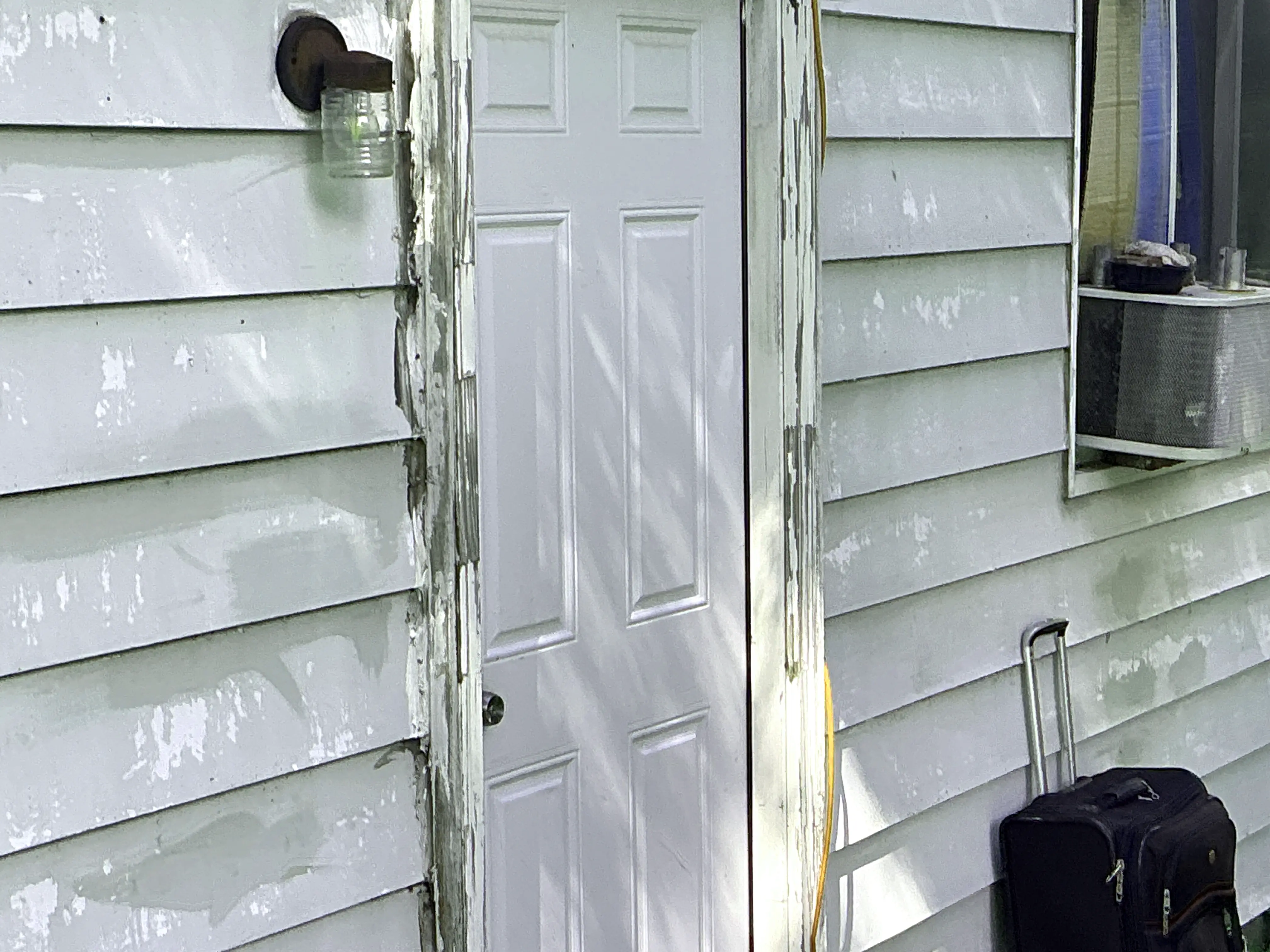 Peeling paint and weathered wood trim around an exterior door on house siding 2026-07-12