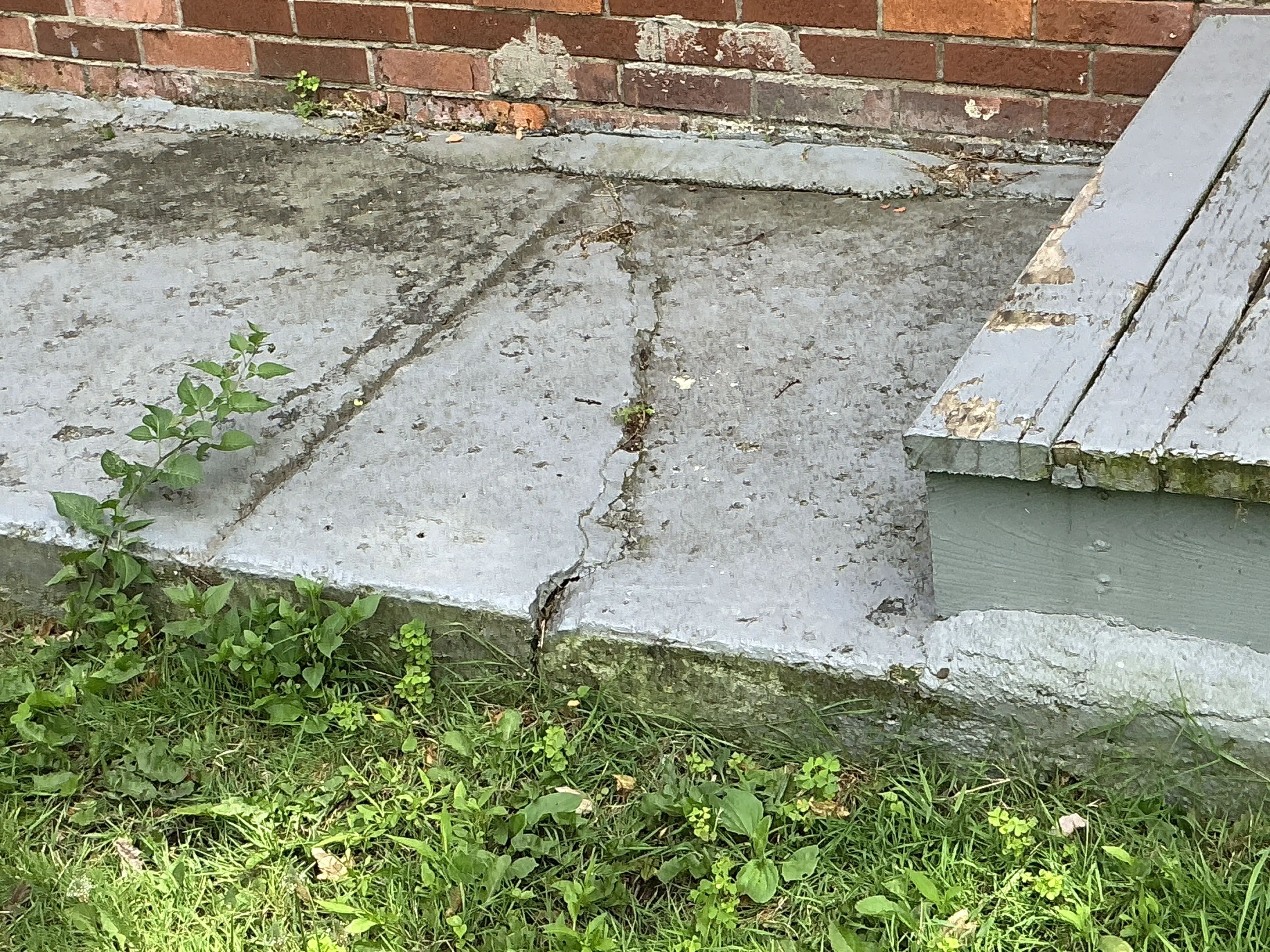 Cracked concrete walkway next to exterior wooden steps and brick wall 2026-08-05