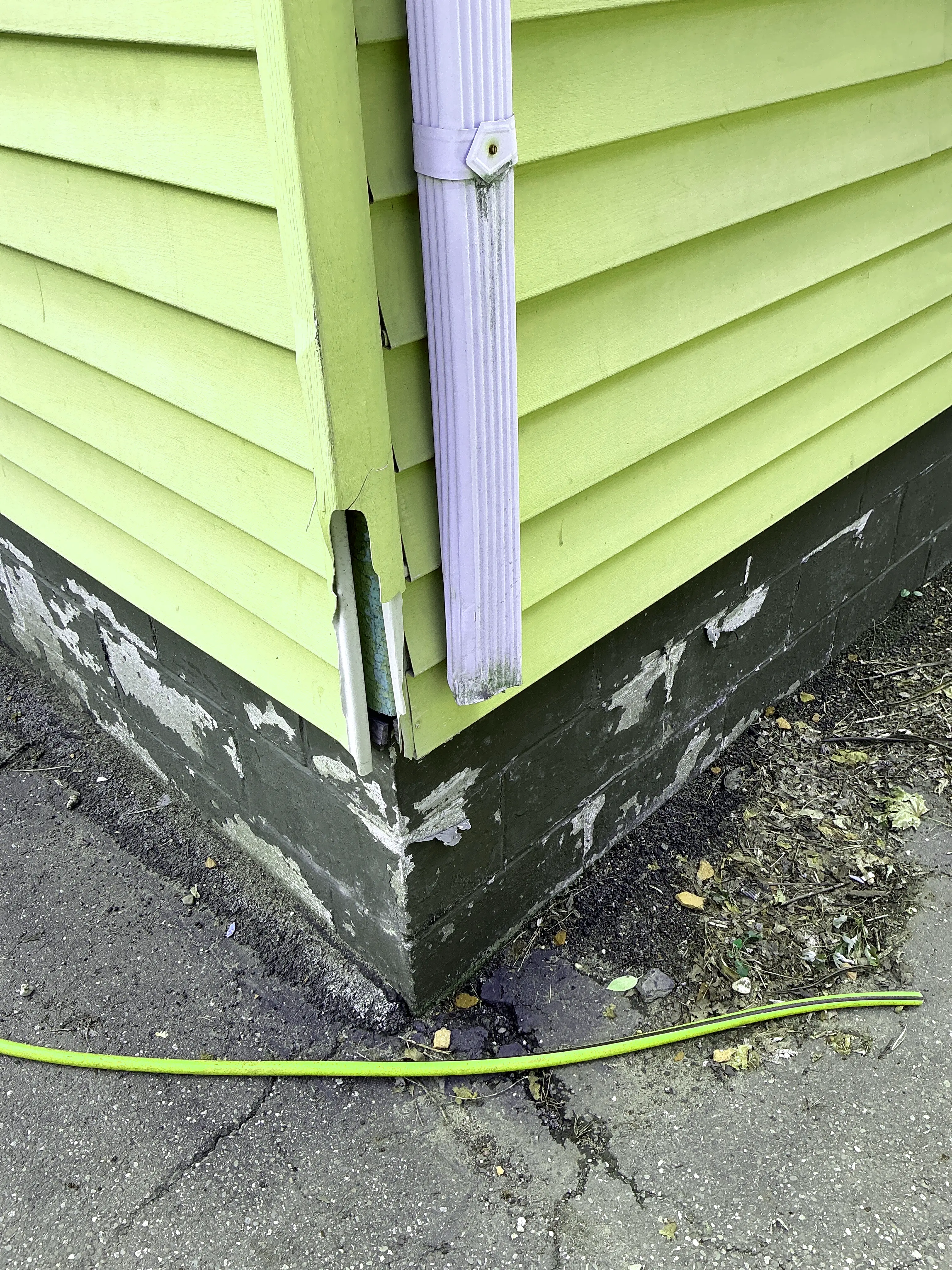 Damaged exterior vinyl siding corner trim and peeling paint on foundation block wall 2026-07-24