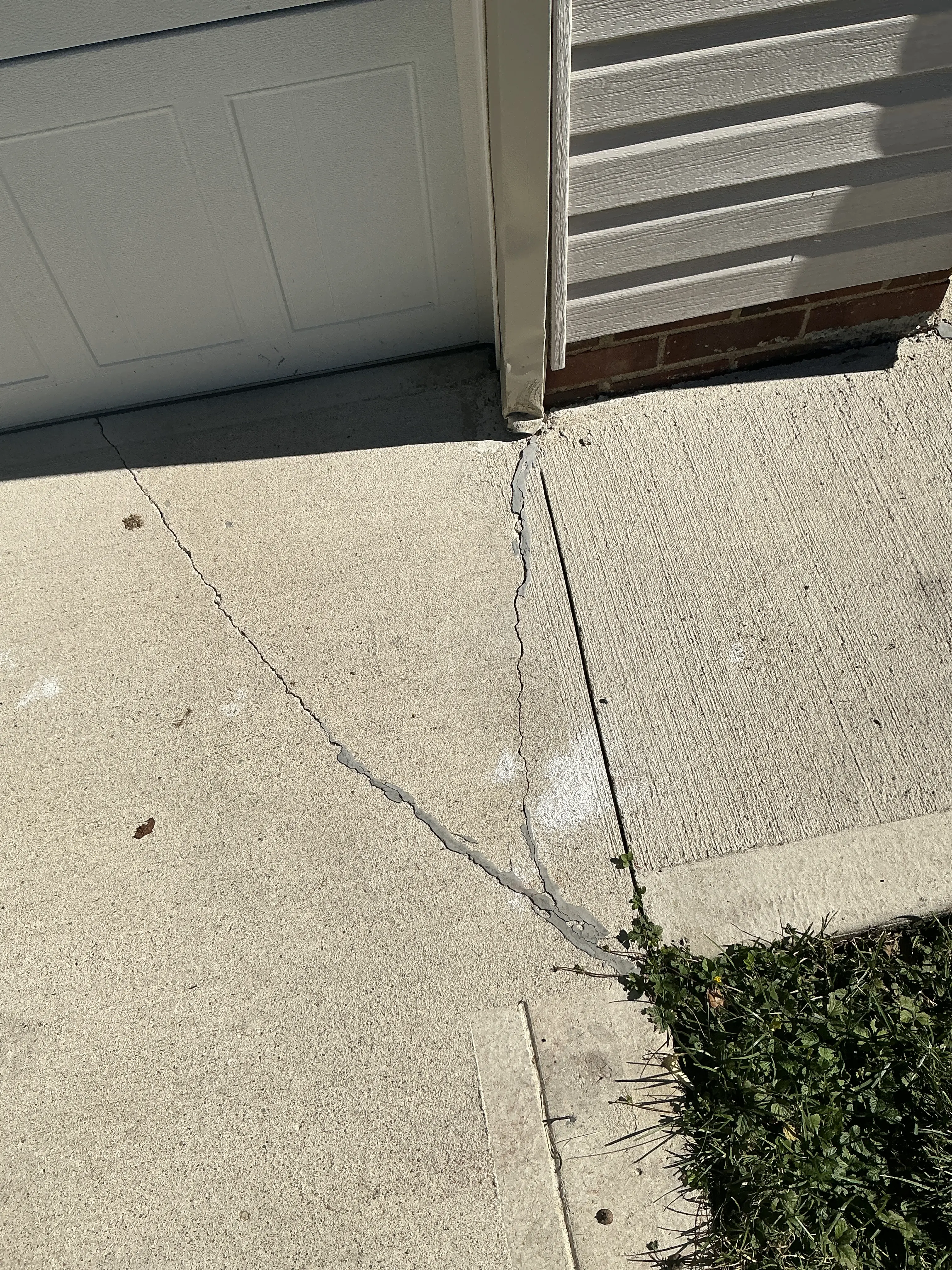 Cracked concrete walkway near house foundation with caulked crack repairs 2026-07-16