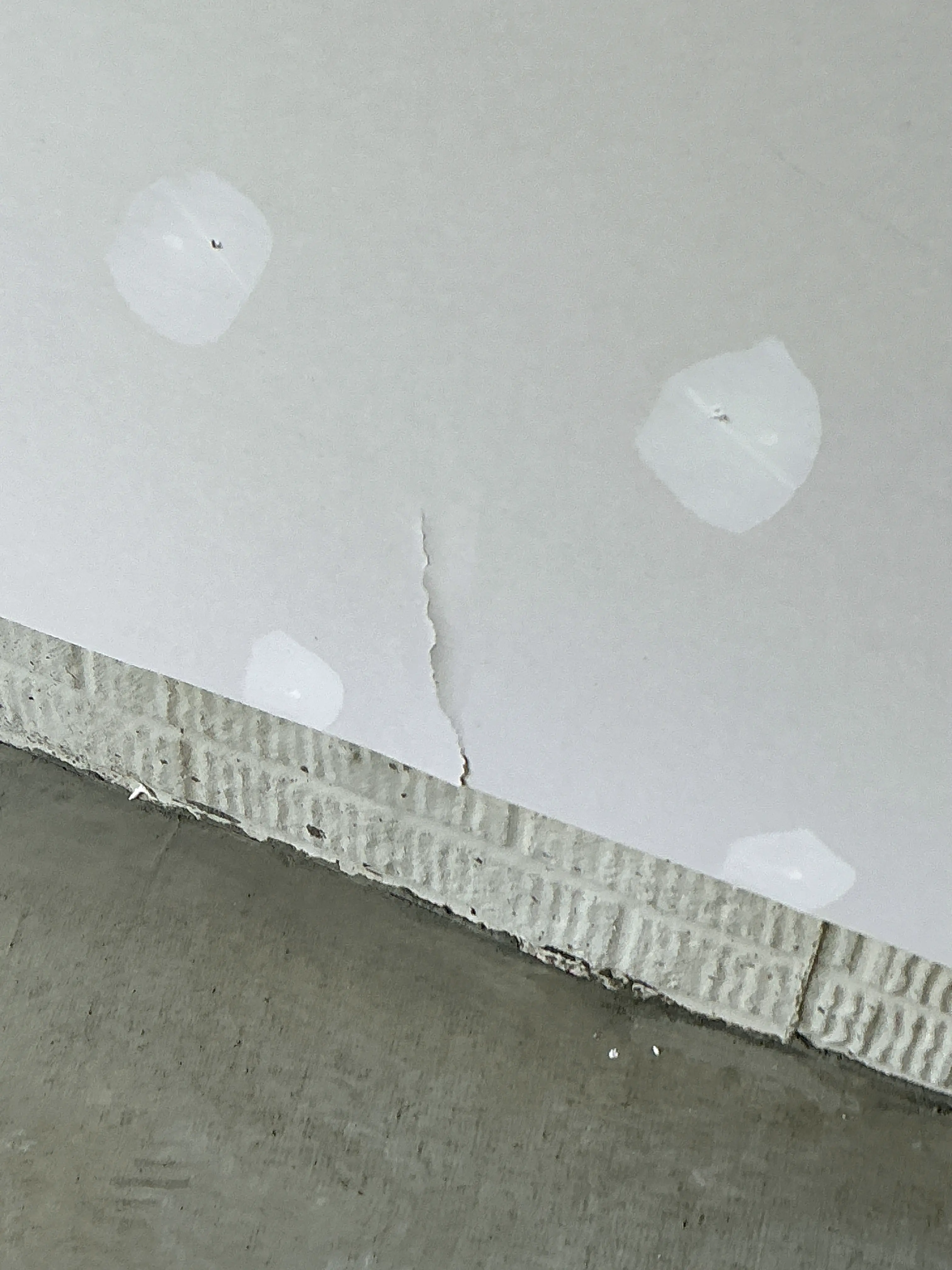 Visible crack in drywall panel near patched screw holes requiring repair 2026-07-08