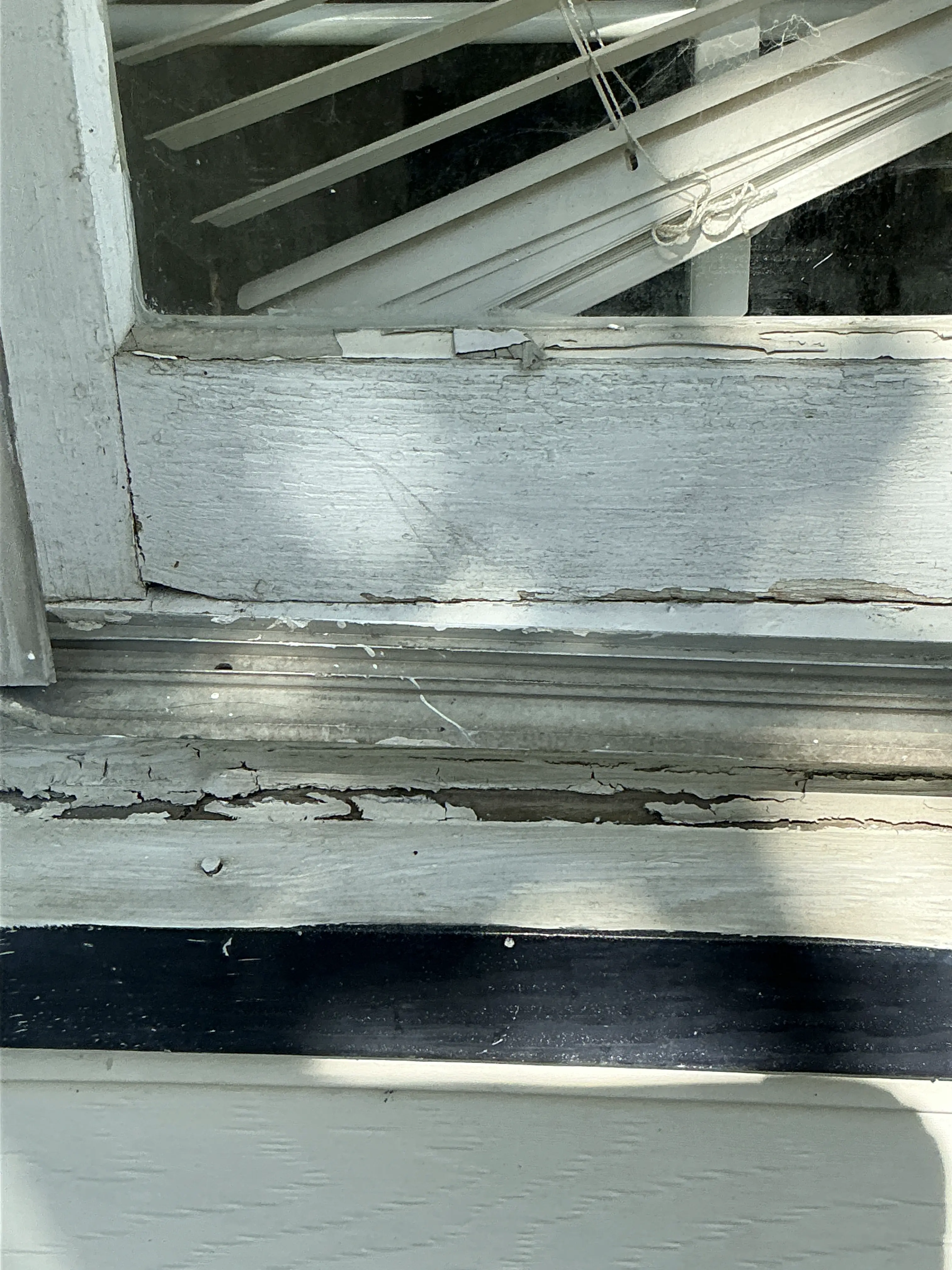 Severely peeling paint and weathered wood frame on an exterior window requiring repair 2026-07-04