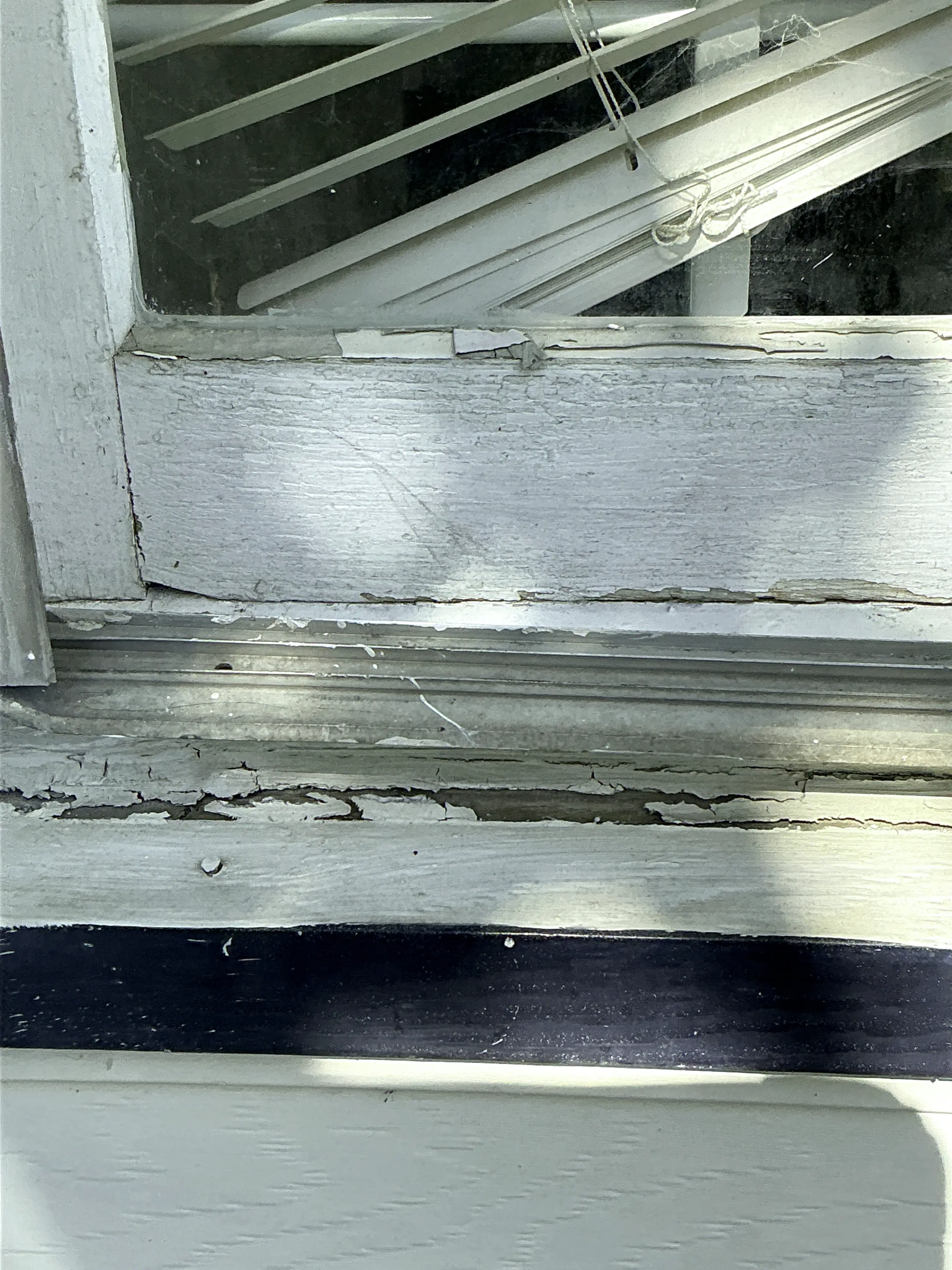 Severely peeling paint and weathered wood frame on an exterior window requiring repair 2026-08-13