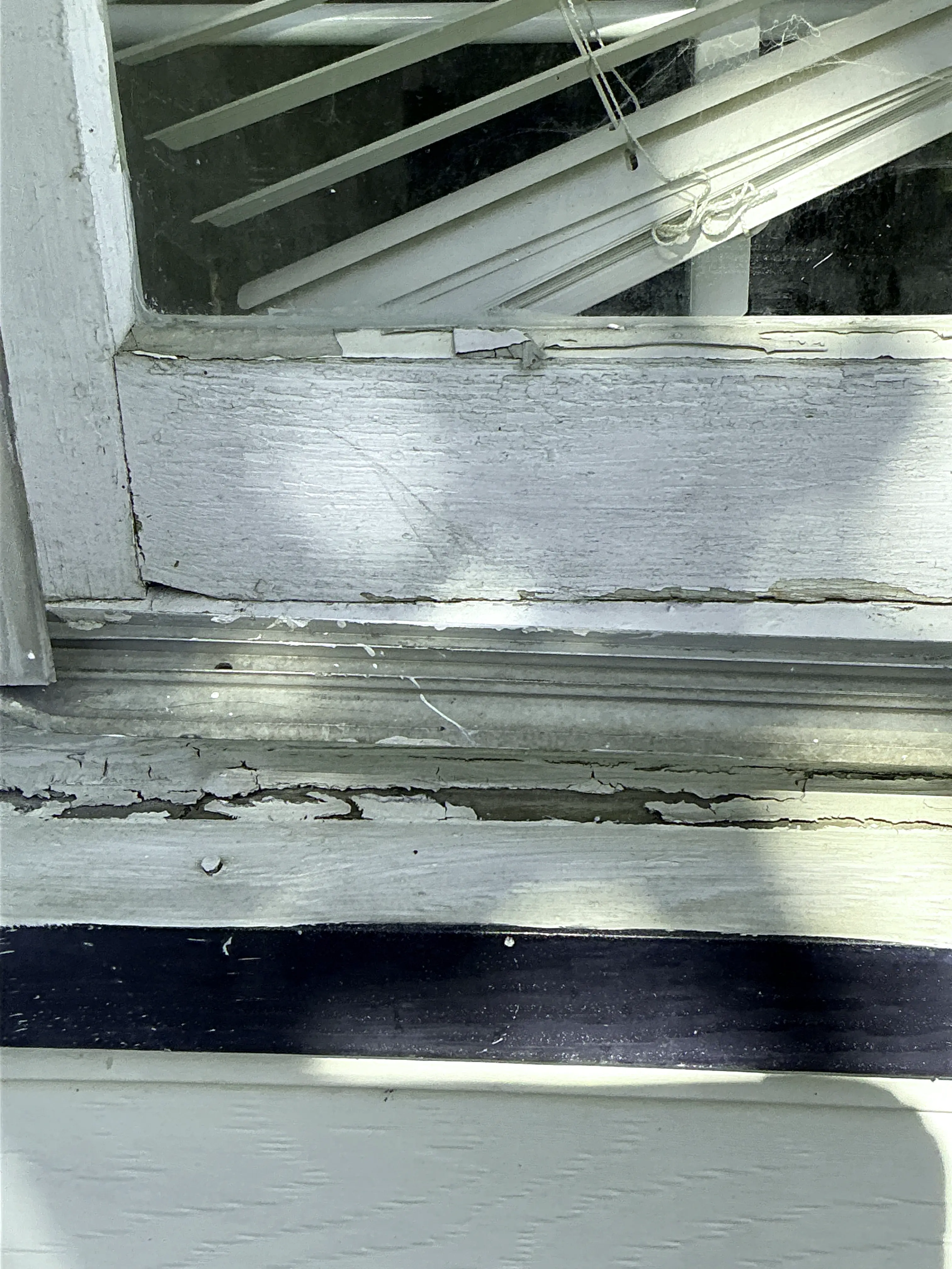 Severely peeling paint and weathered wood frame on an exterior window requiring repair 2026-08-21