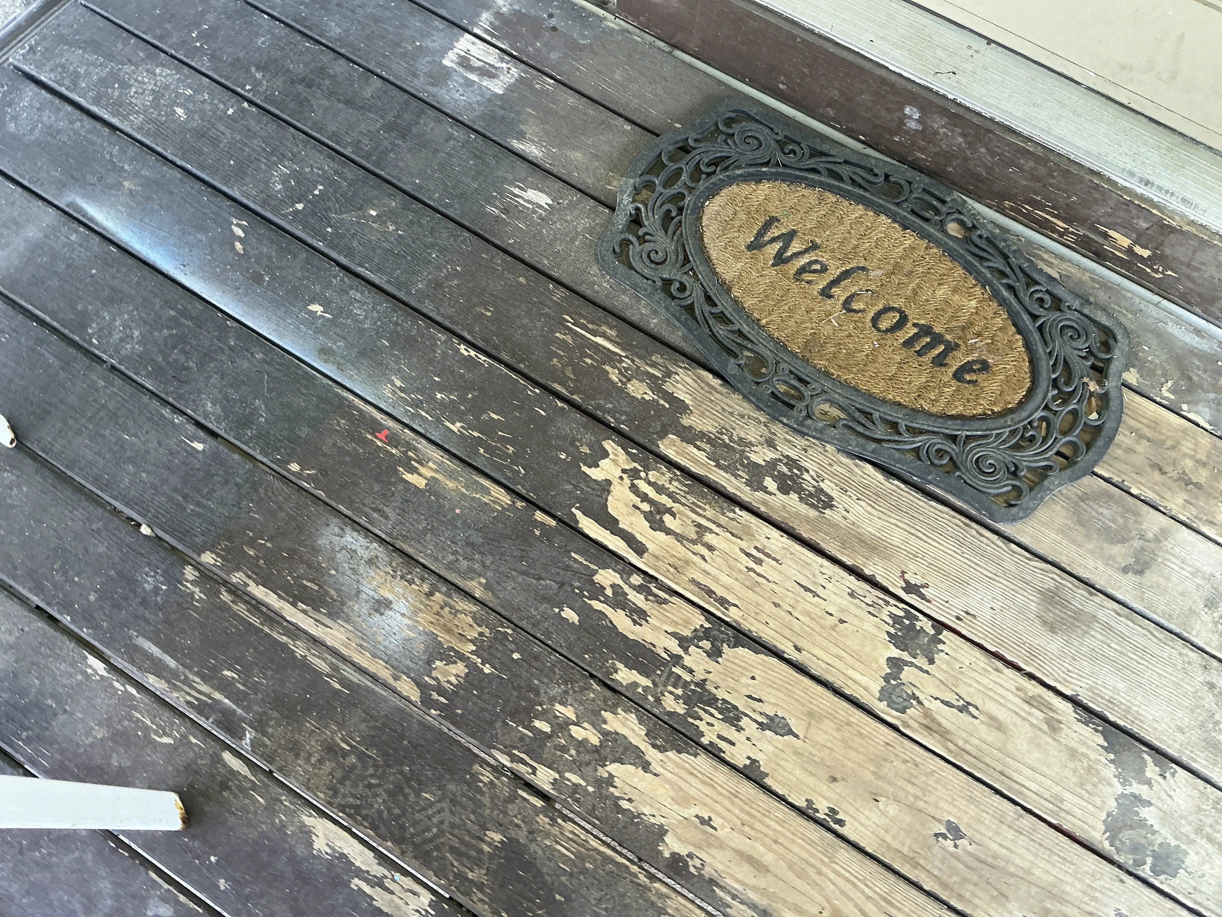 Peeling stain and weathered wooden porch deck boards near entryway 2026-07-24