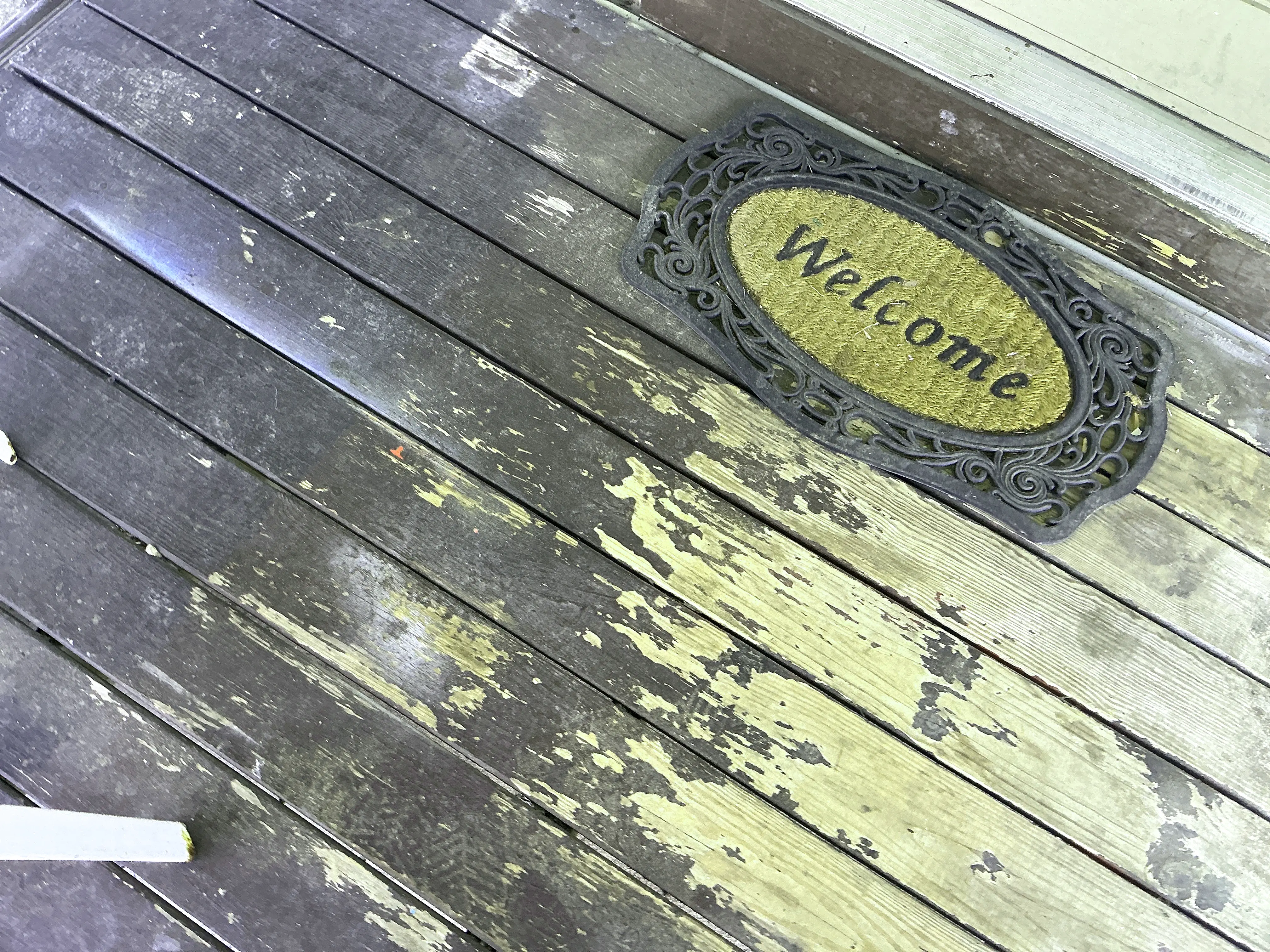 Peeling stain and weathered wooden porch deck boards near entryway 2026-07-05