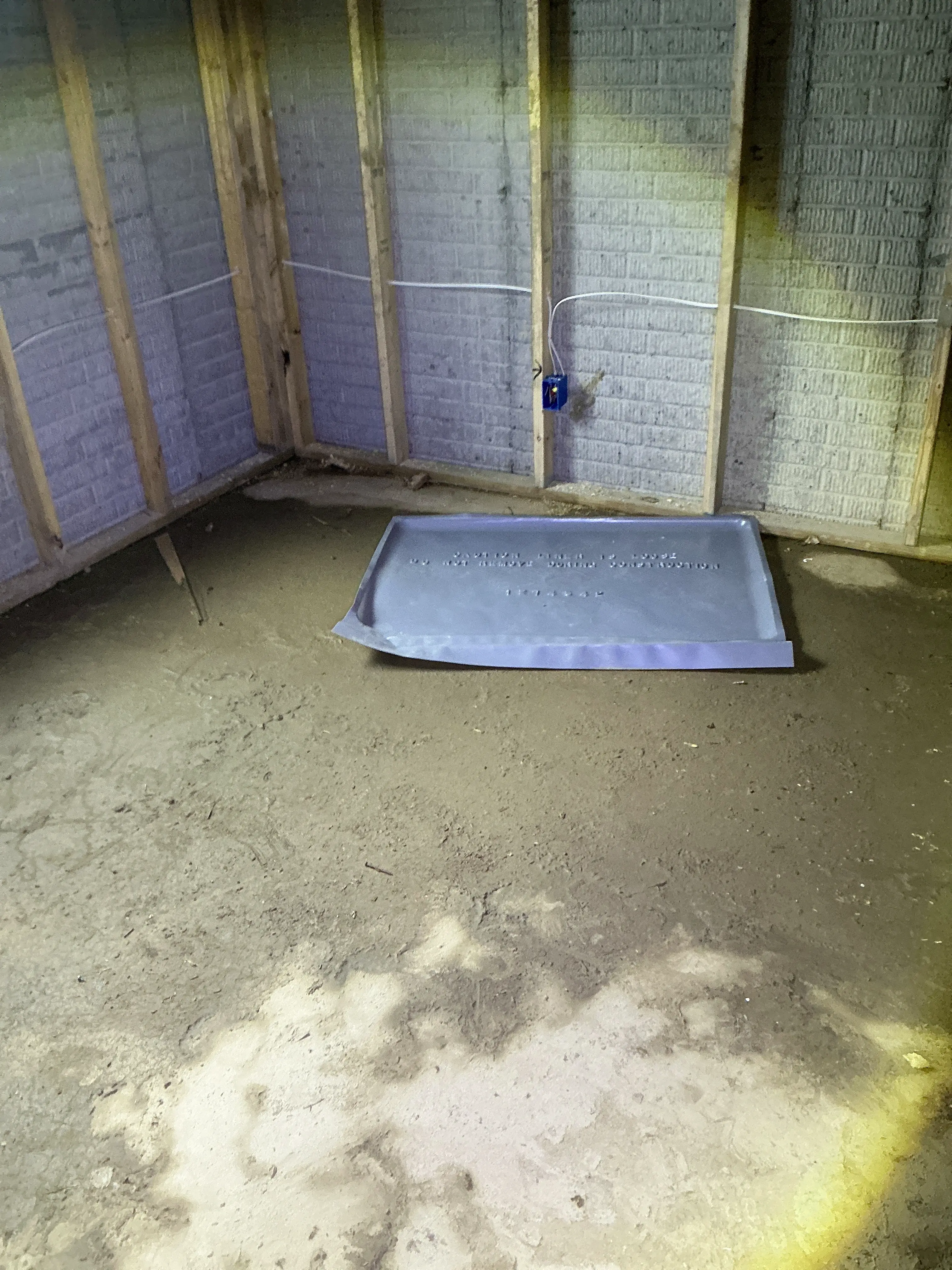 Unfinished basement dirt floor with exposed wall framing, electrical junction box, and plastic pan. 2026-07-12