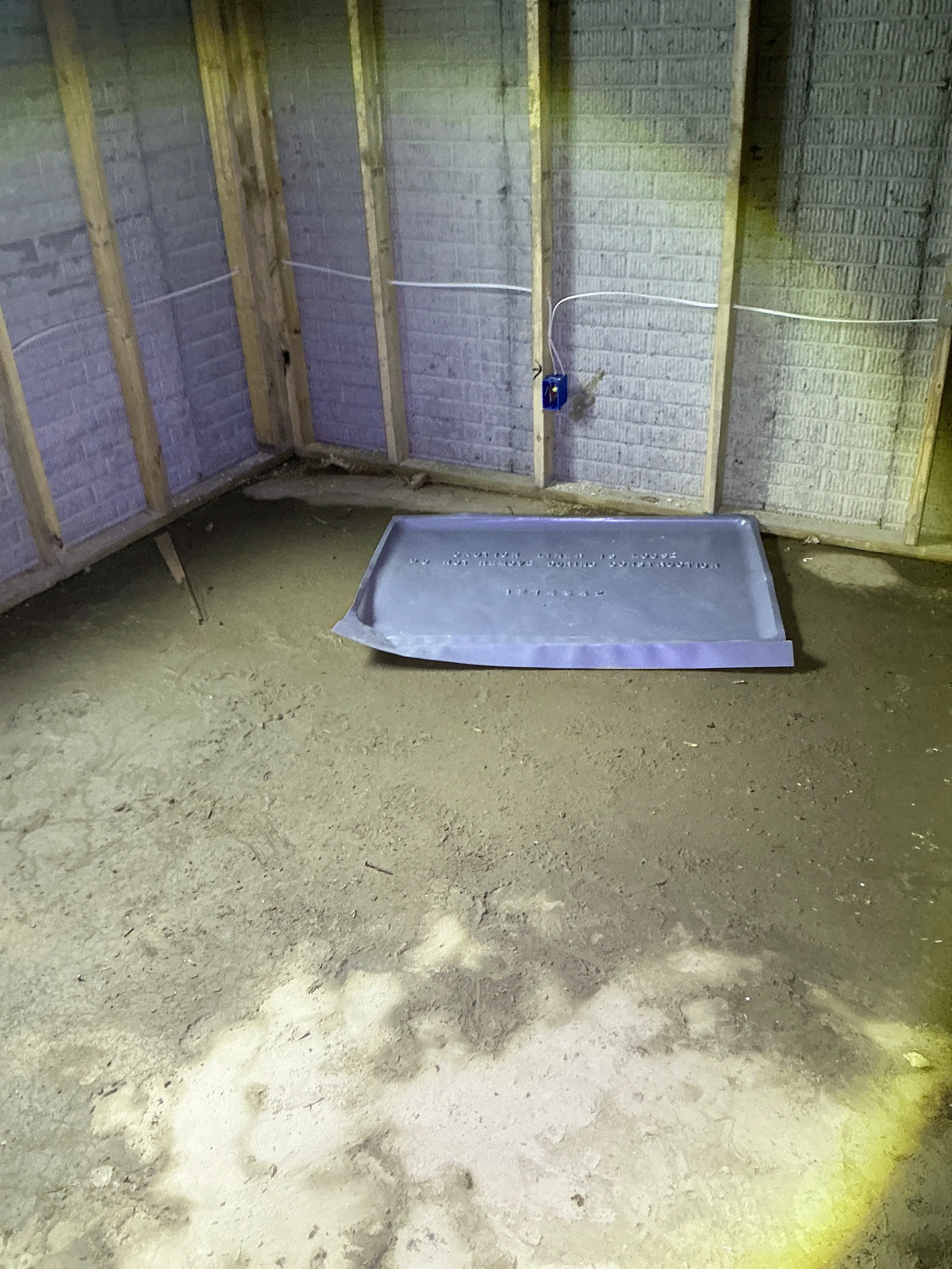 Unfinished basement dirt floor with exposed wall framing, electrical junction box, and plastic pan. 2026-08-12