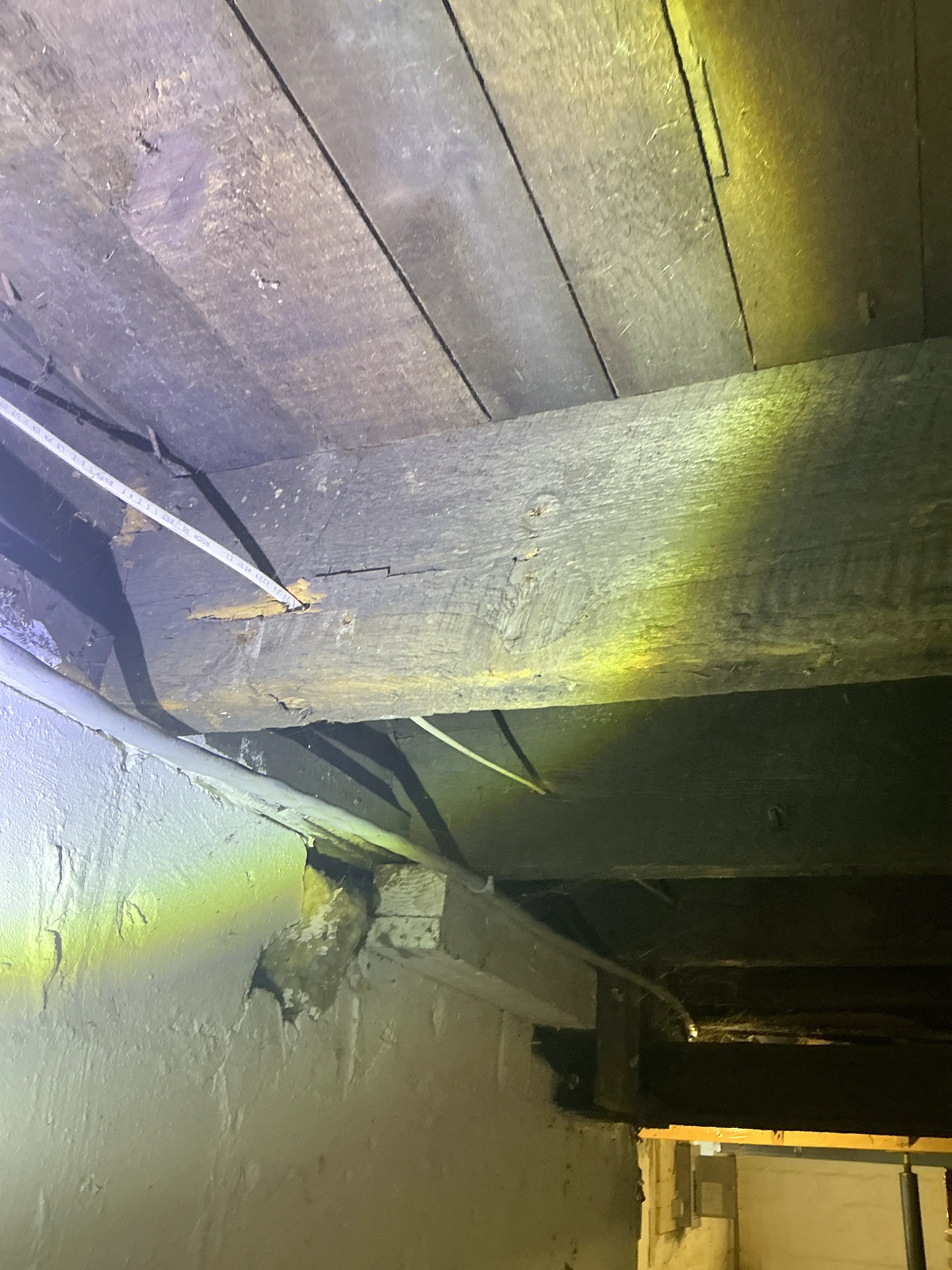 Electrical wiring routed through wooden beam in dark crawlspace during home inspection 2026-07-06