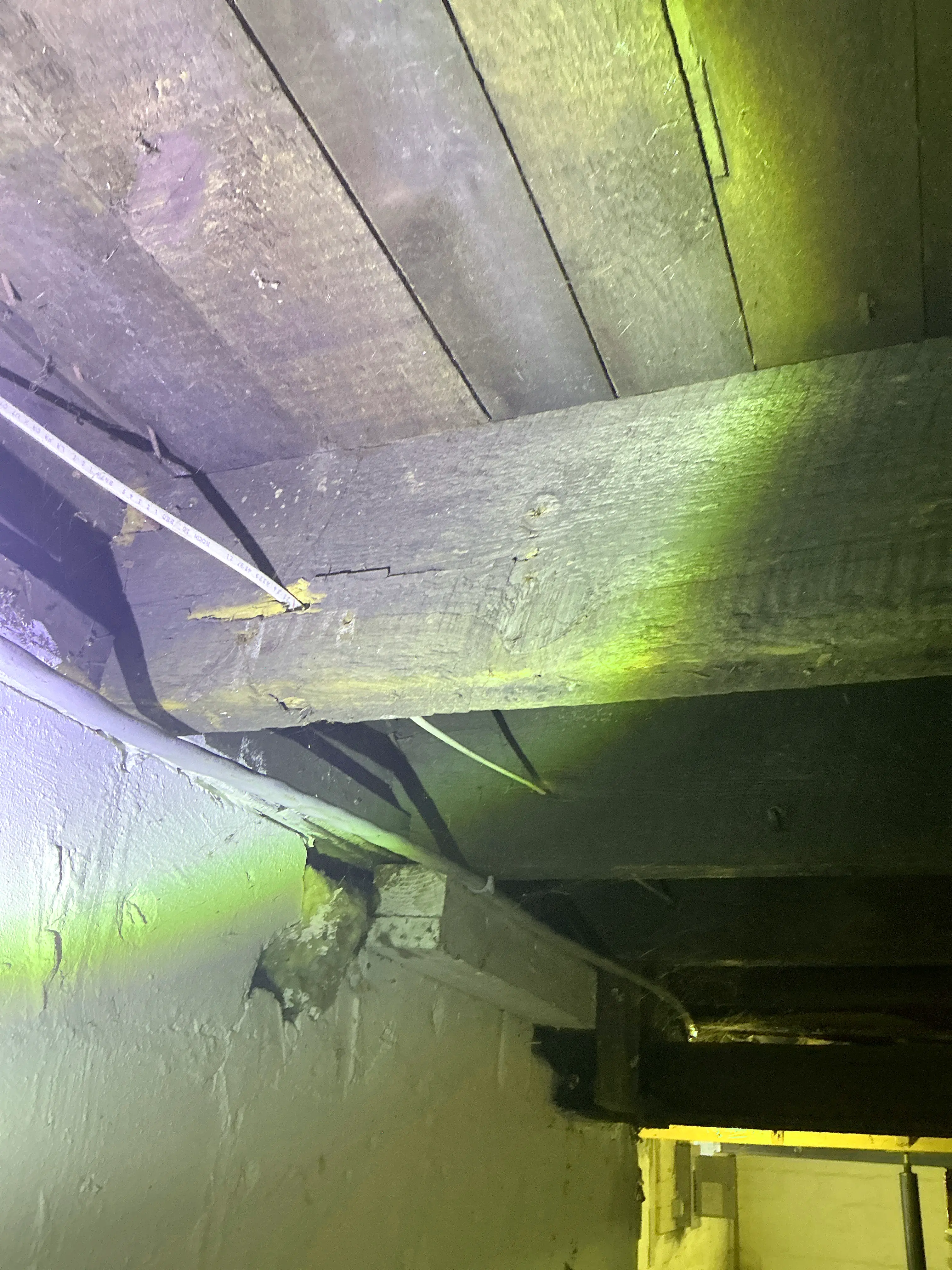 Electrical wiring routed through wooden beam in dark crawlspace during home inspection 2026-07-13