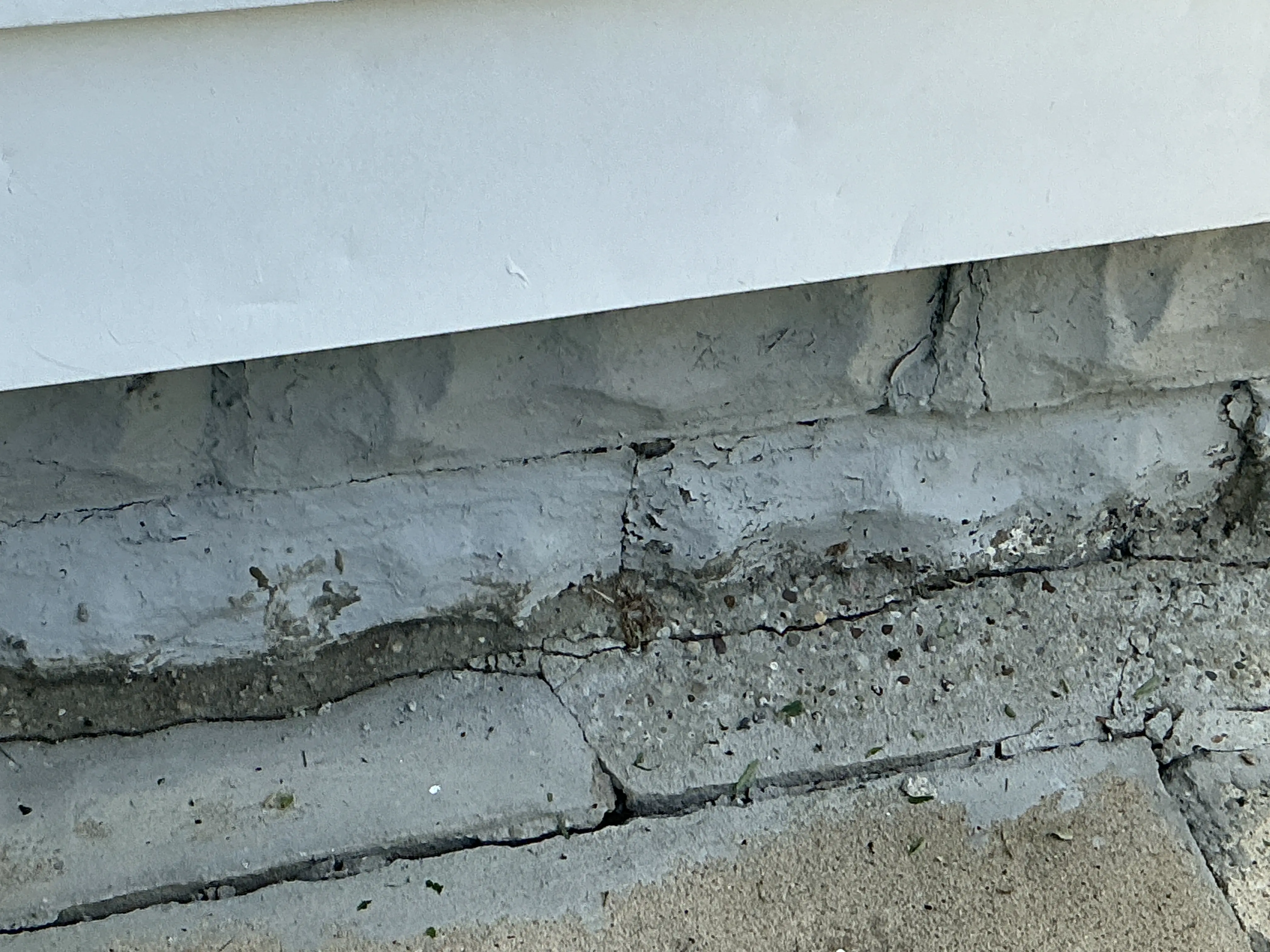 Cracked concrete foundation wall beneath white siding showing signs of deterioration and settlement 2026-08-16