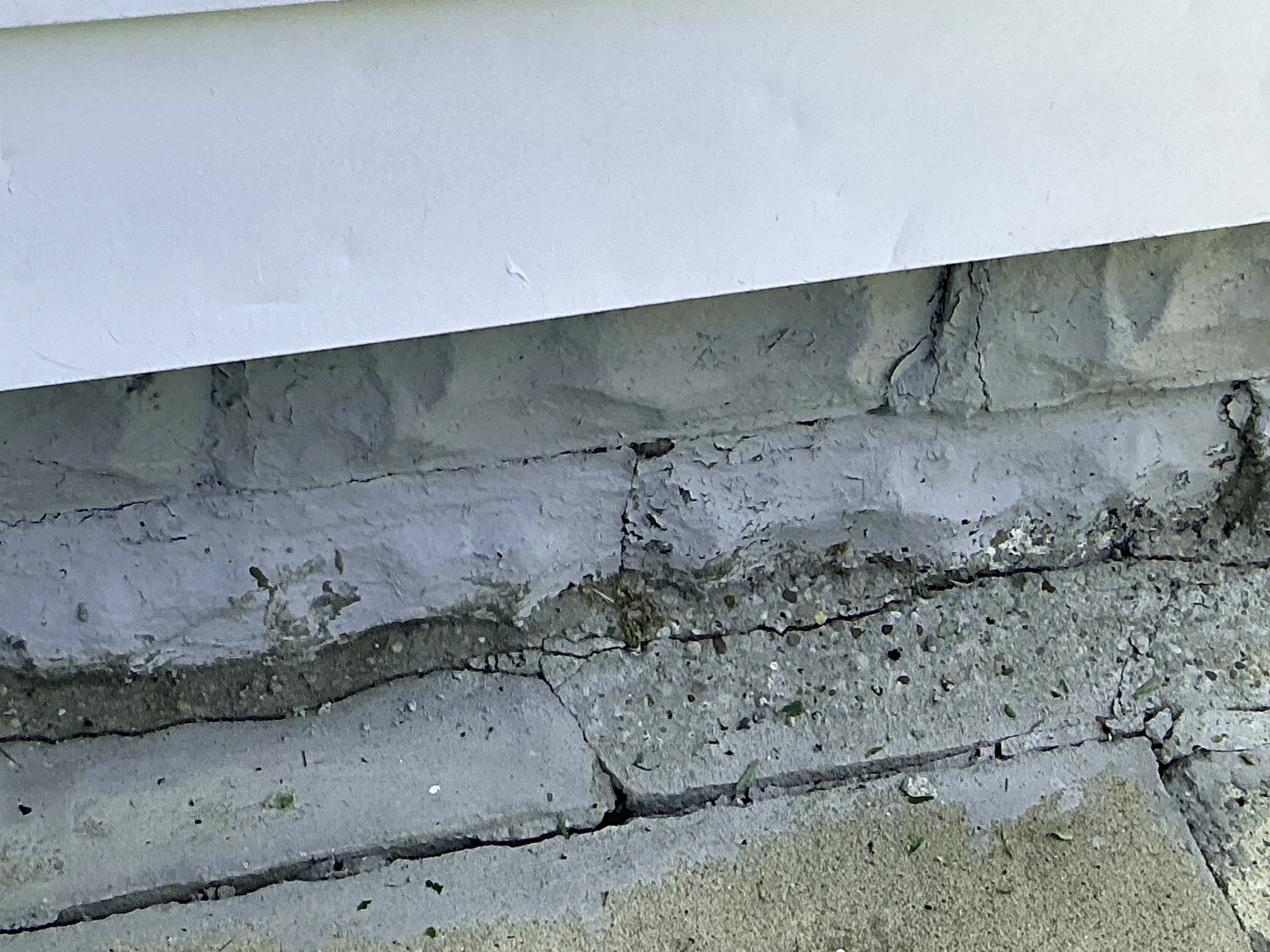 Cracked concrete foundation wall beneath white siding showing signs of deterioration and settlement 2026-08-15